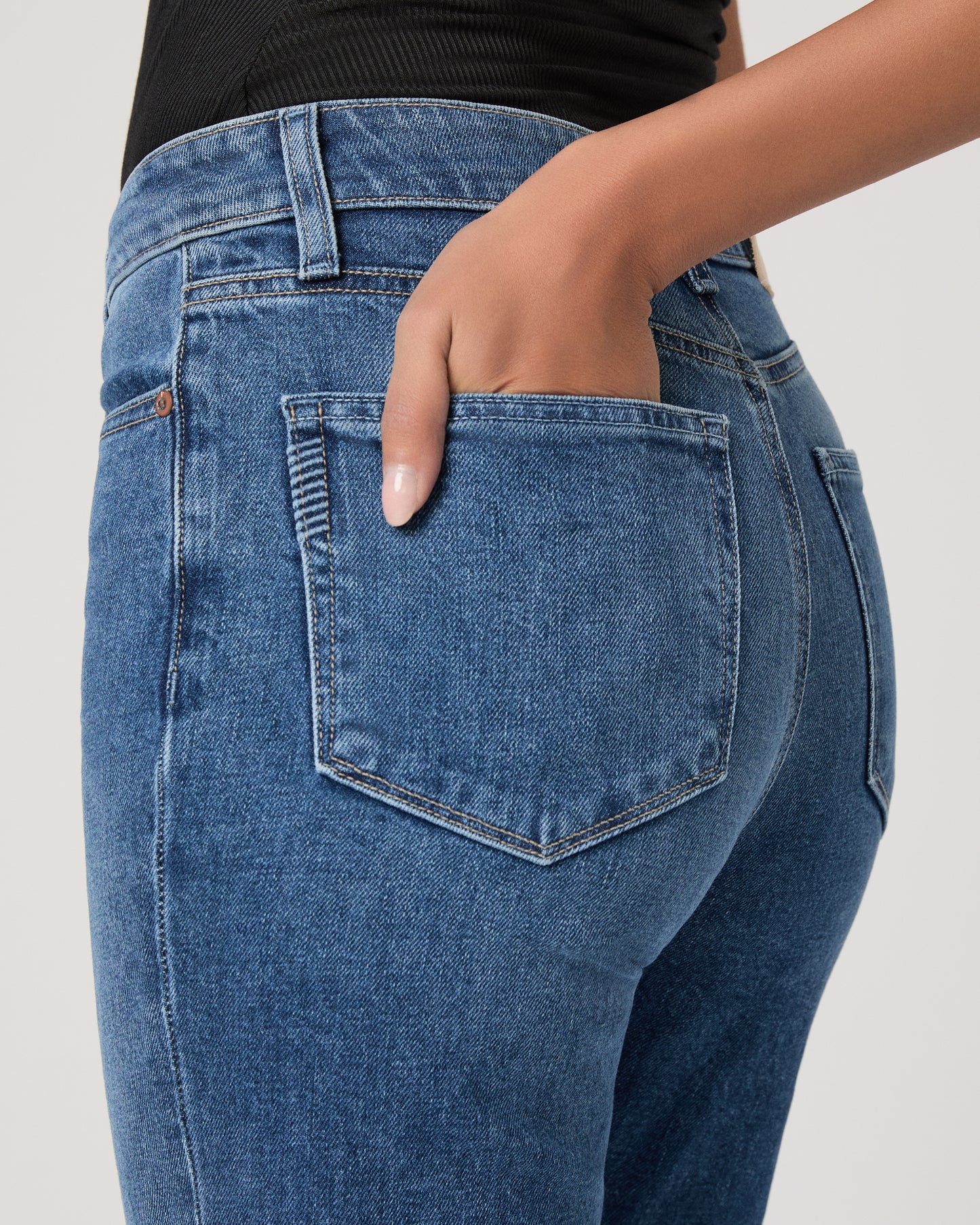 Woman wearing a black sleeveless top and blue jeans on a white background