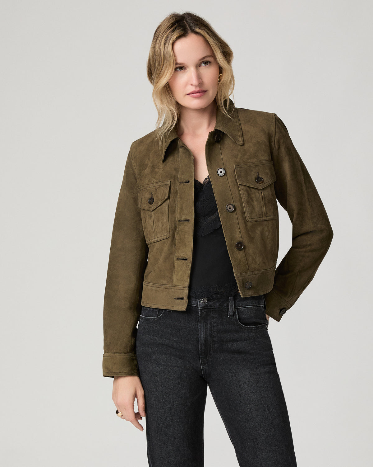 Close-up front view of a woman wearing the open rich olive suede Feyd Jacket over a black top, showing the cargo chest pockets and belt detail.