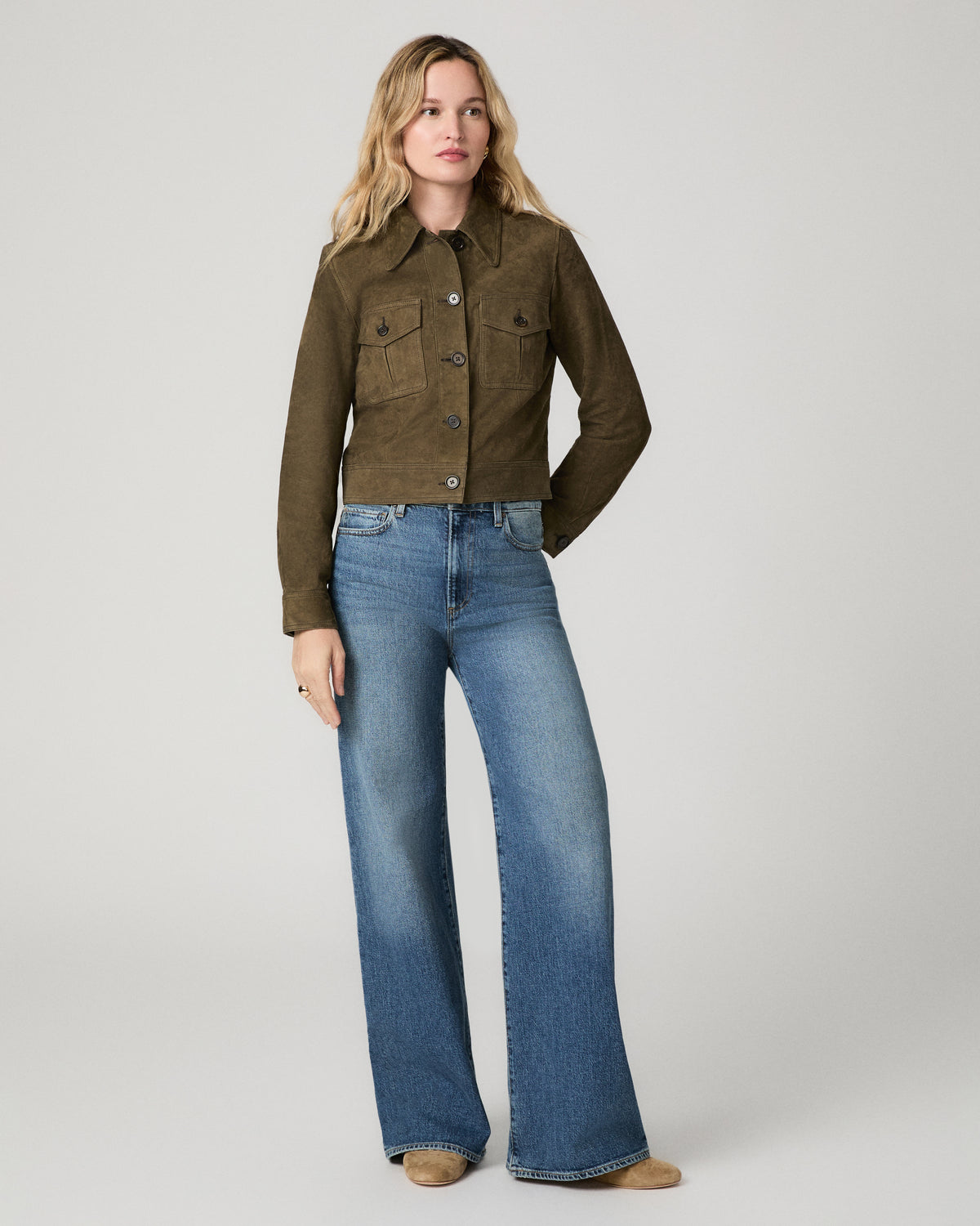 Full-length front view of a woman wearing the rich olive suede Feyd Jacket over wide-leg denim jeans with tan boots.