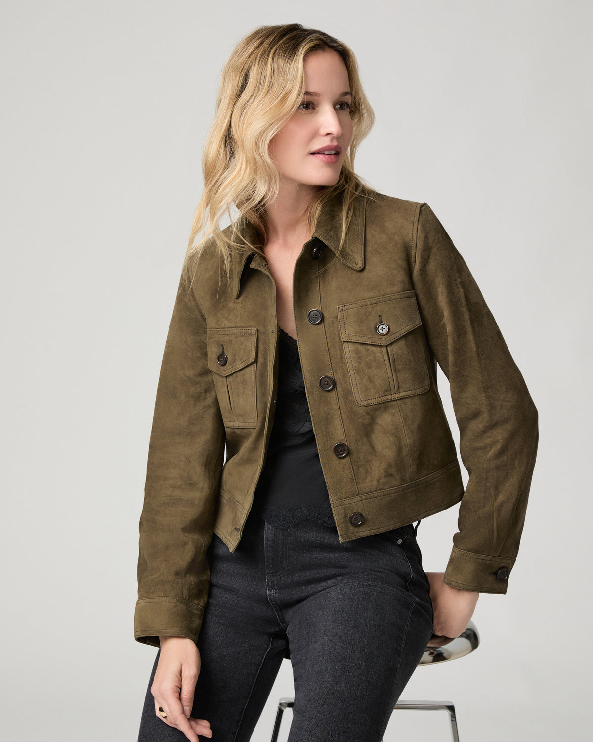 Close-up front view of a woman wearing the buttoned rich olive suede Feyd Jacket, hand near the collar.