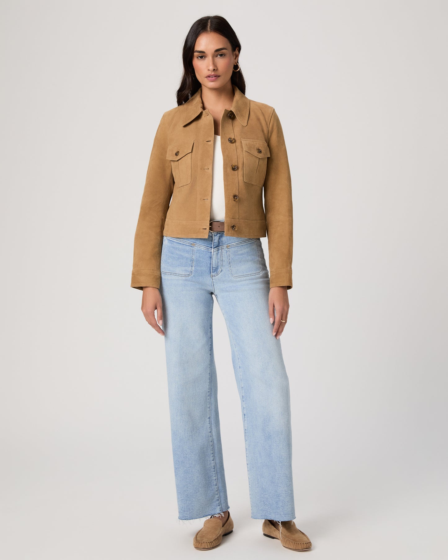 Woman wearing a brown jacket and light blue jeans on a plain background