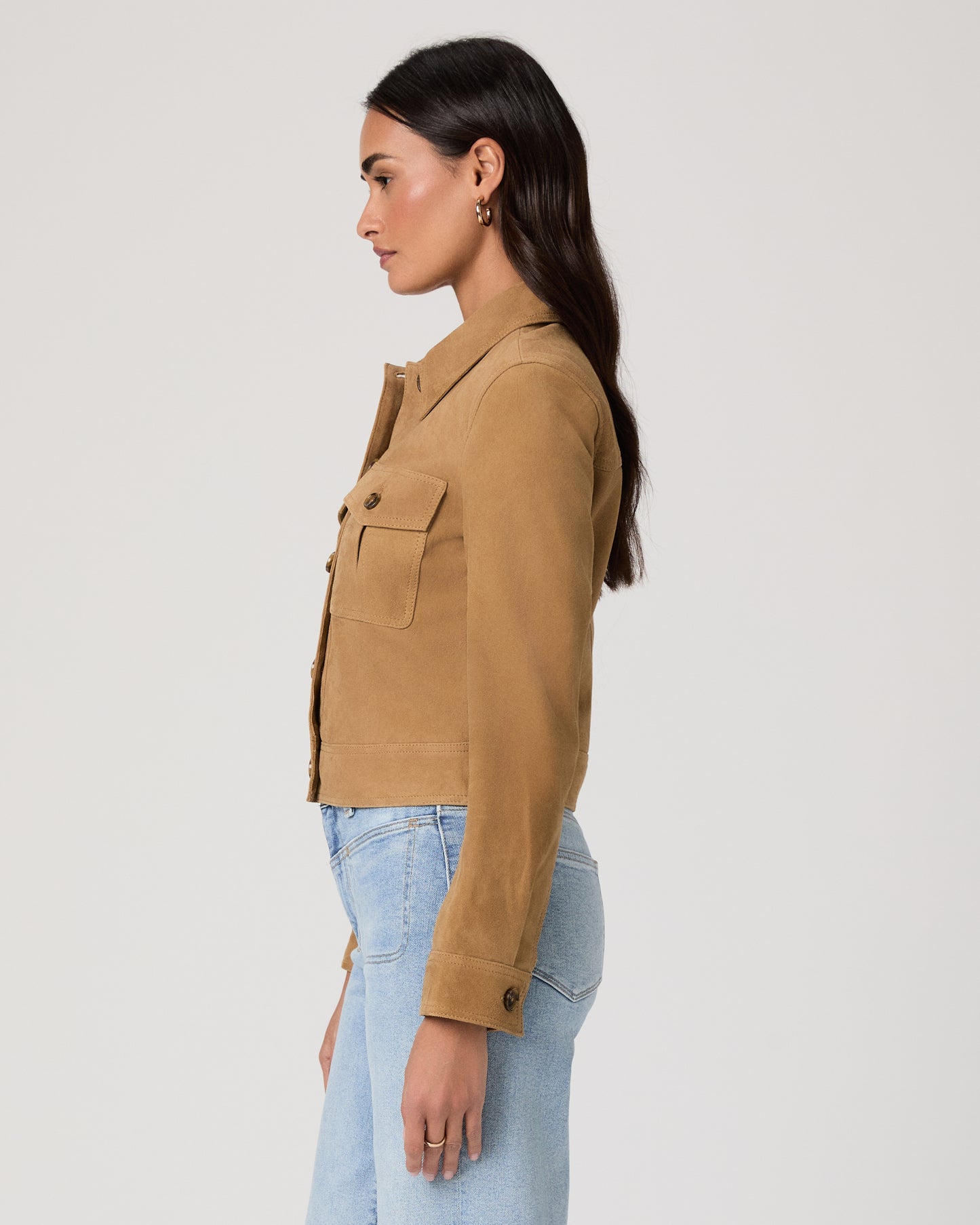 Woman wearing a brown jacket and light blue jeans on a plain background