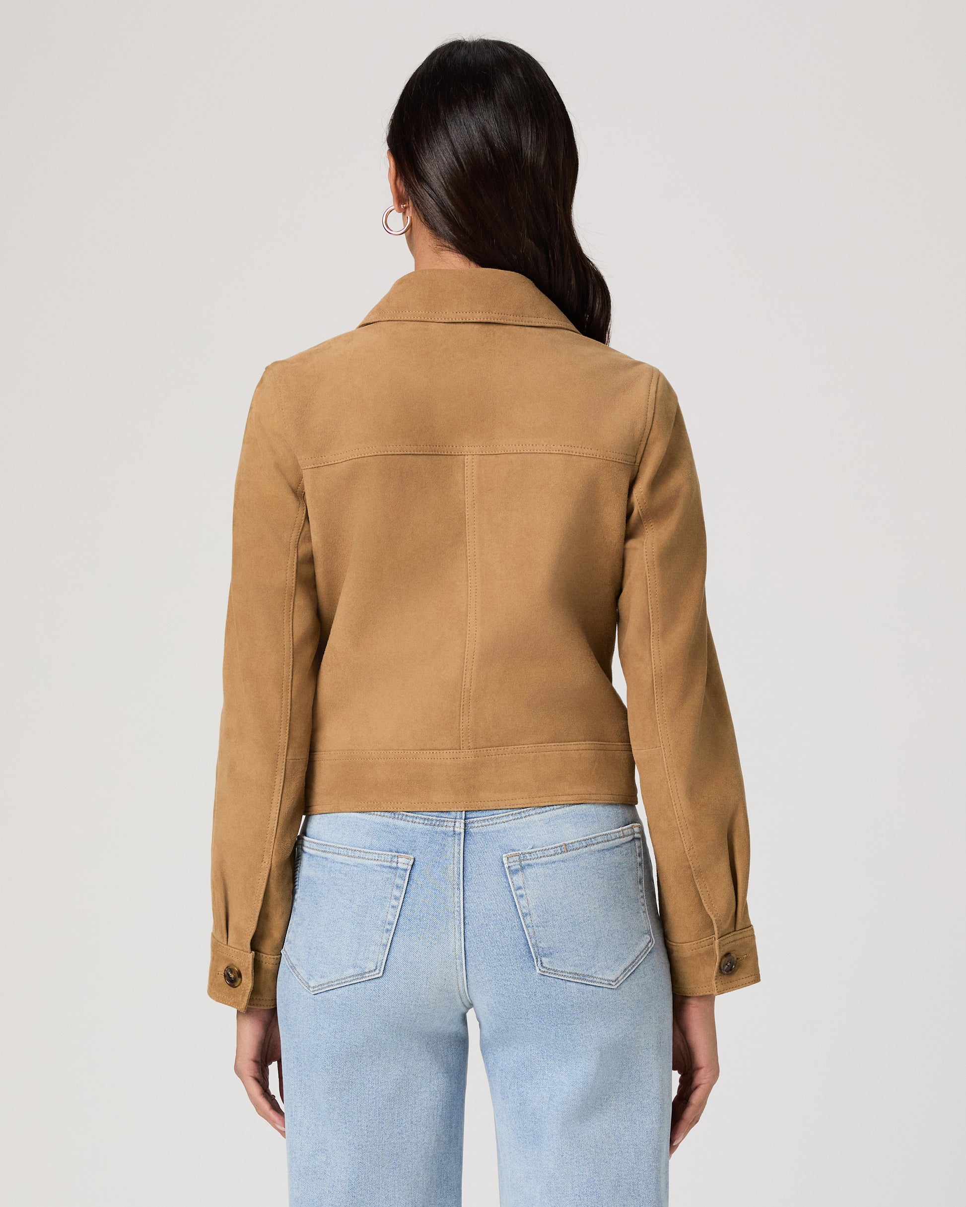 Woman wearing a brown jacket and light blue jeans on a plain background