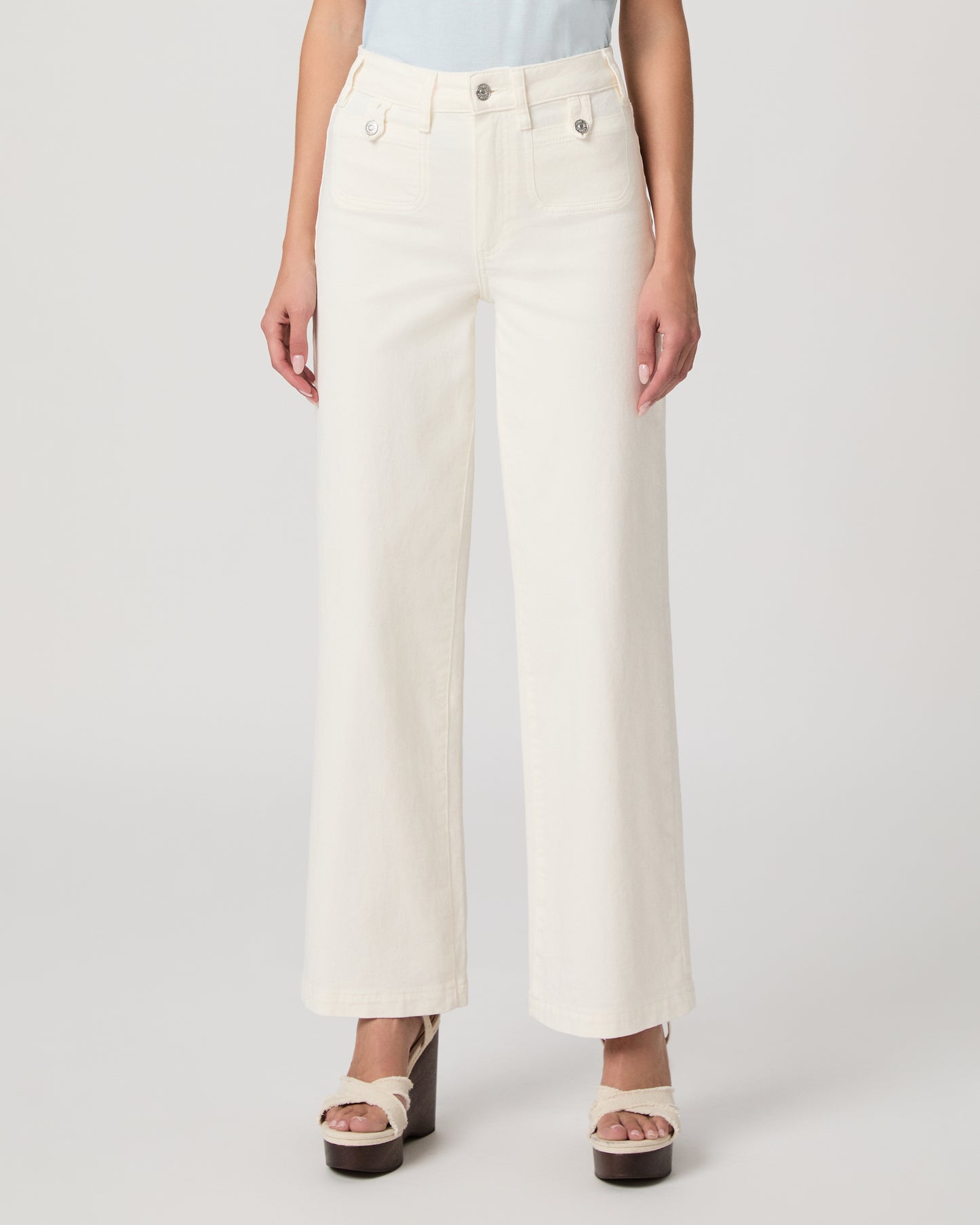 Woman wearing a light blue top paired with a white flare denim on a white background