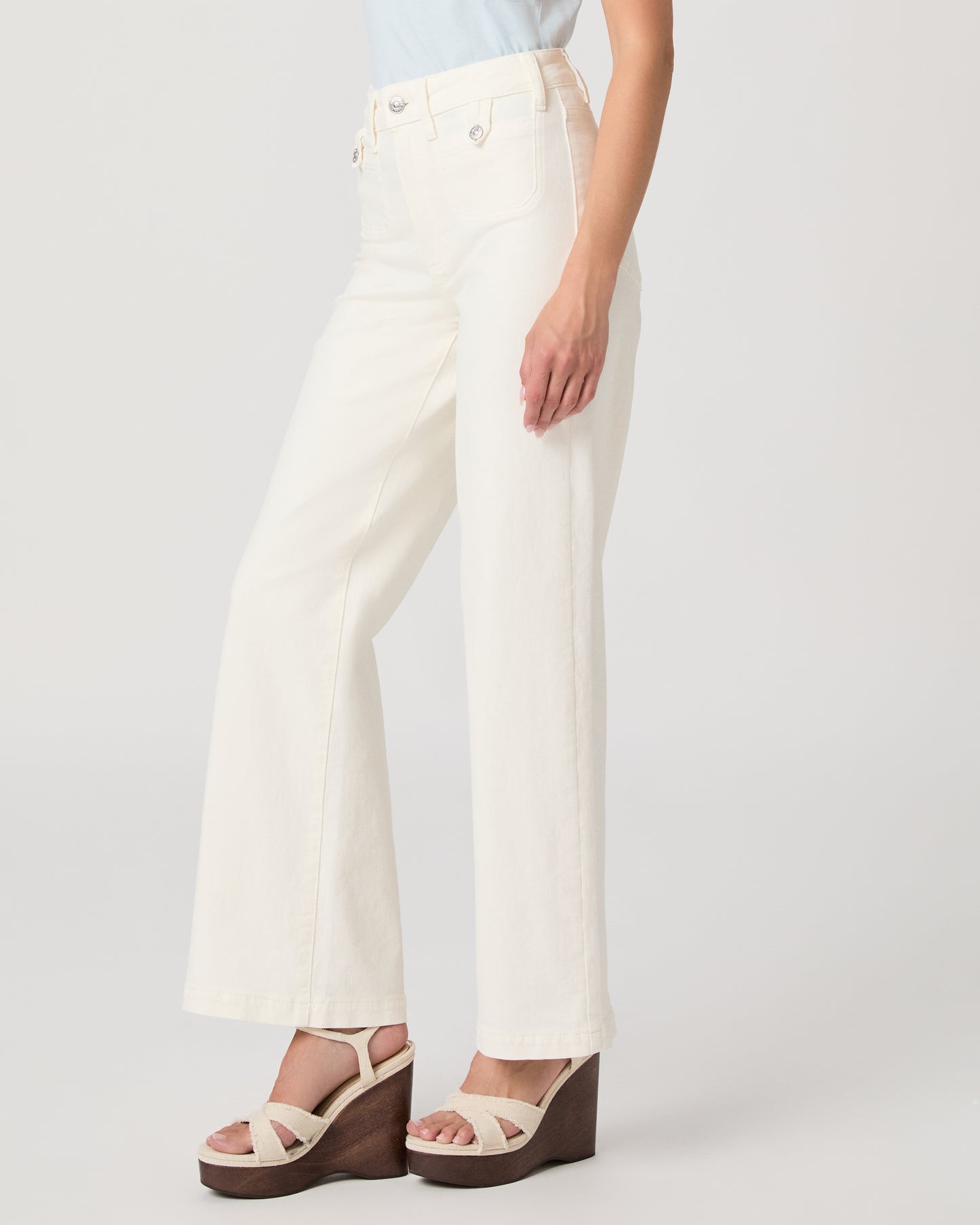 Woman wearing a light blue top paired with a white flare denim on a white background