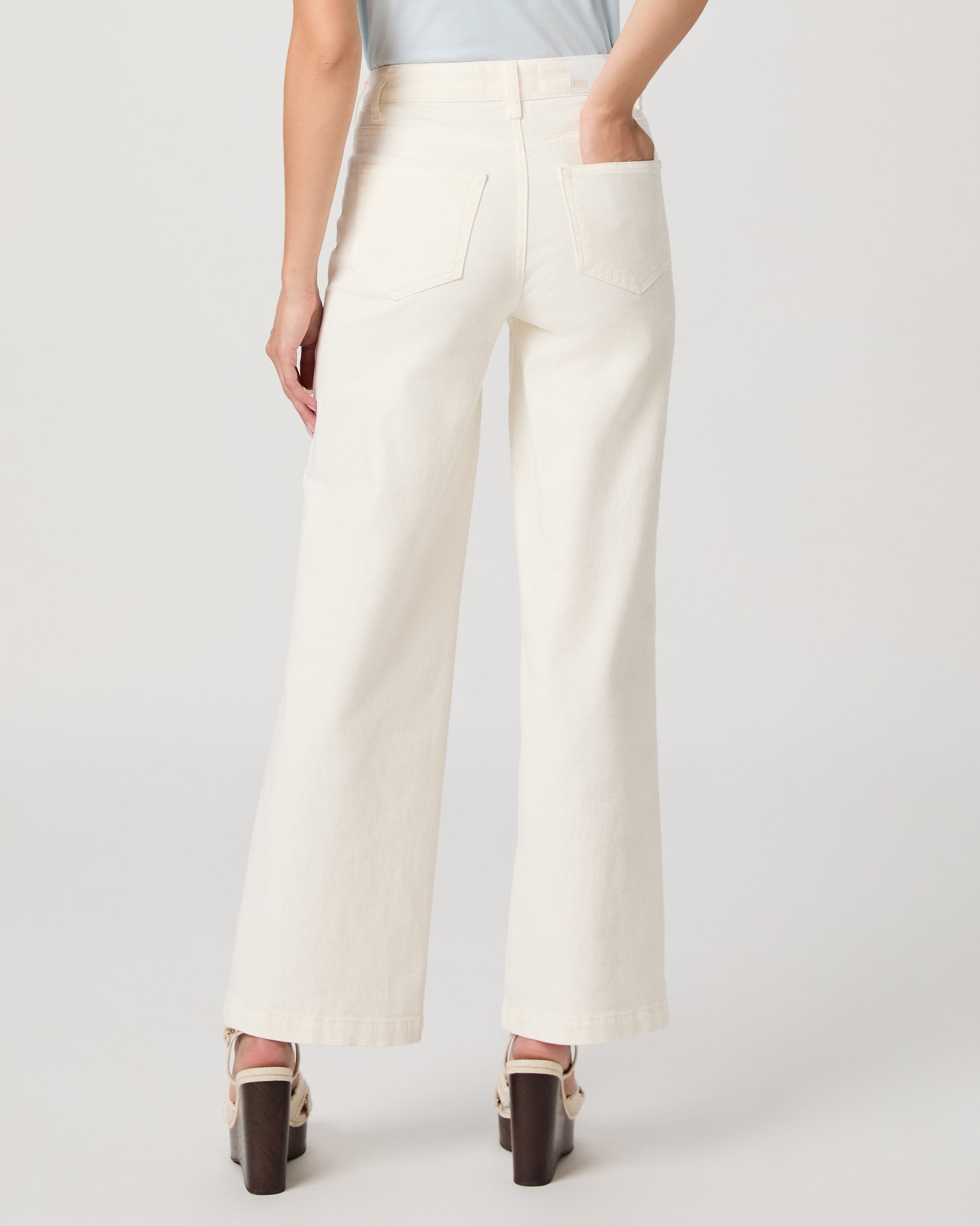 Woman wearing a light blue top paired with a white flare denim on a white background