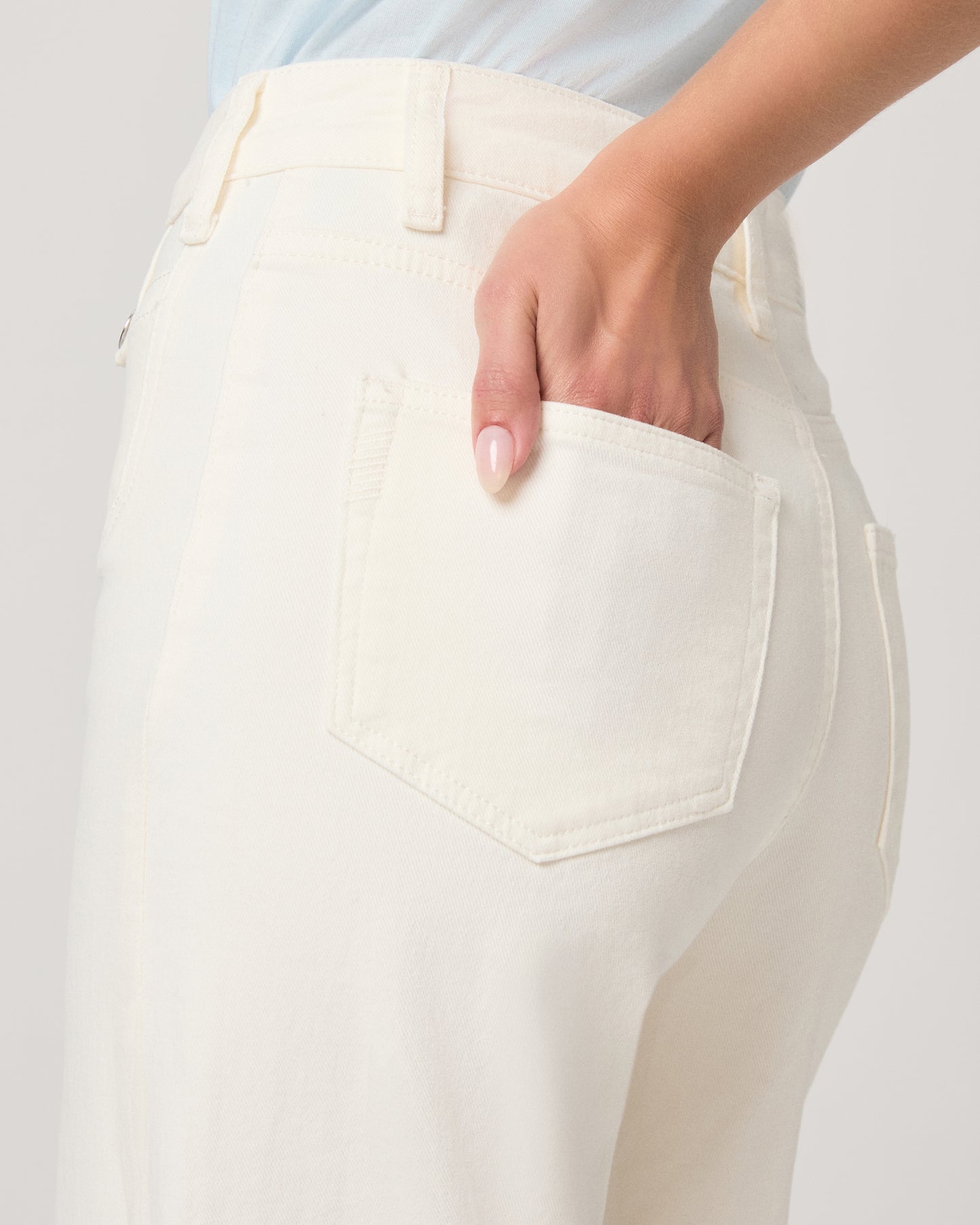 Woman wearing a light blue top paired with a white flare denim on a white background