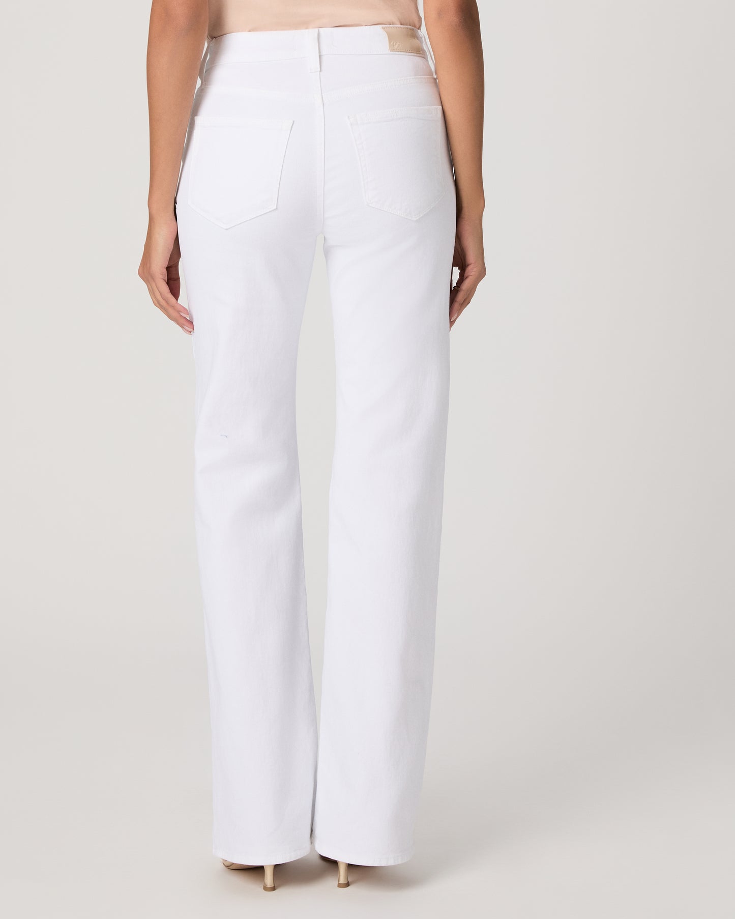 Woman wearing a light pink sleeveless top and white pants paired with gold sandals on a plain background