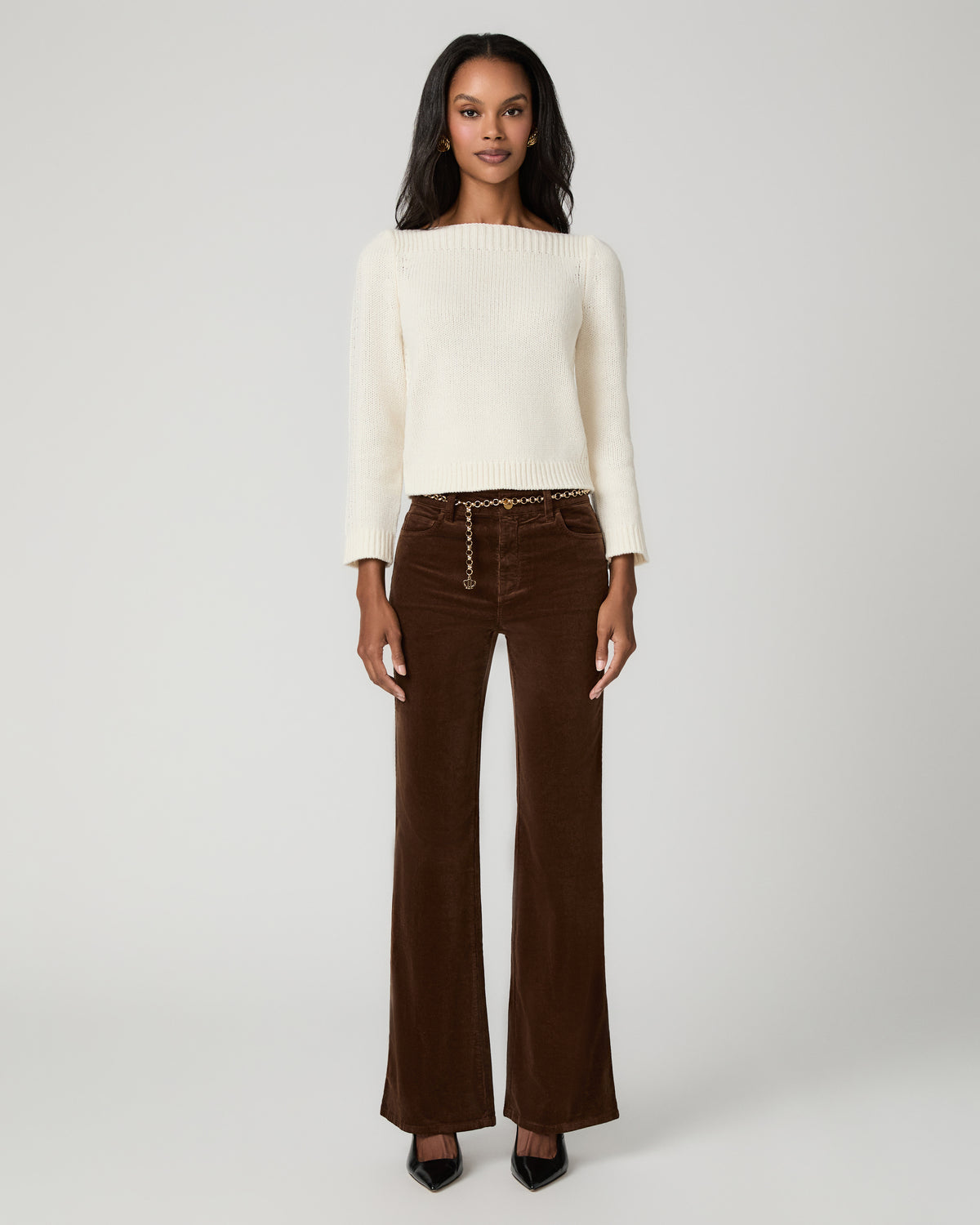 Full-length front view of a woman wearing an ivory sweater and hickory brown corduroy flare pants with button-front detail, paired with black pointed-toe heels.