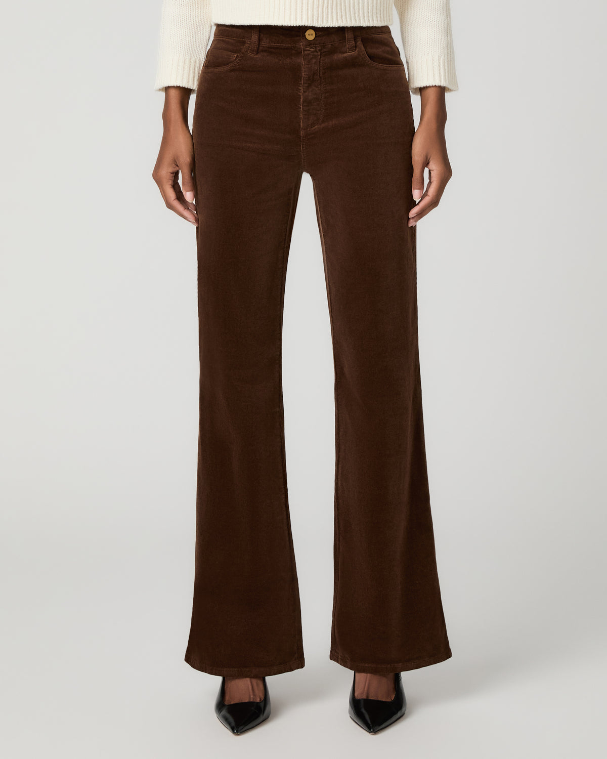 Close-up front view of hickory brown corduroy flare pants with a button waistband, styled with an ivory sweater and black pointed-toe heels.