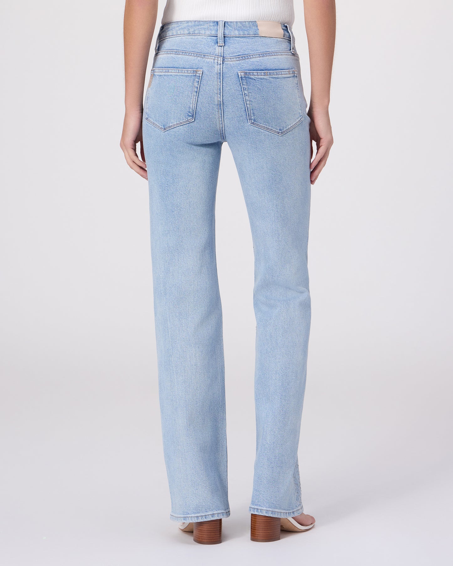 Woman wearing a white sleeveless top and light blue jeans on a white background