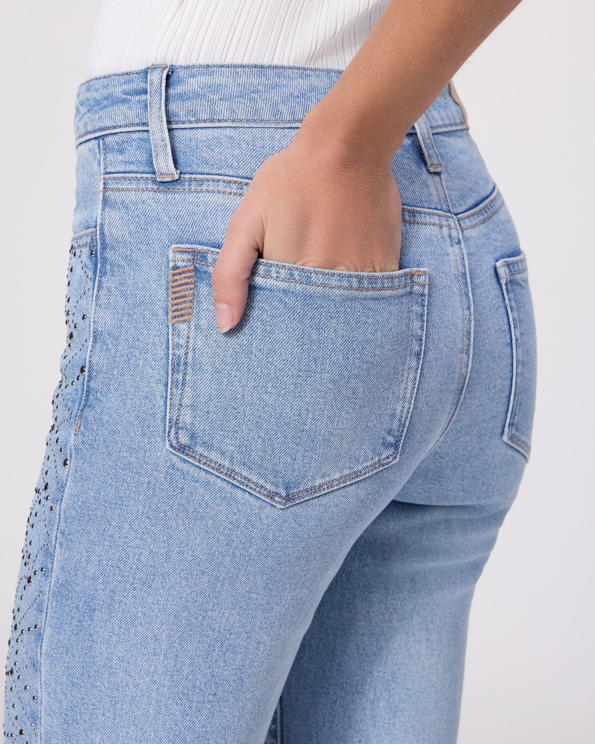 Woman wearing a white sleeveless top and light blue jeans on a white background