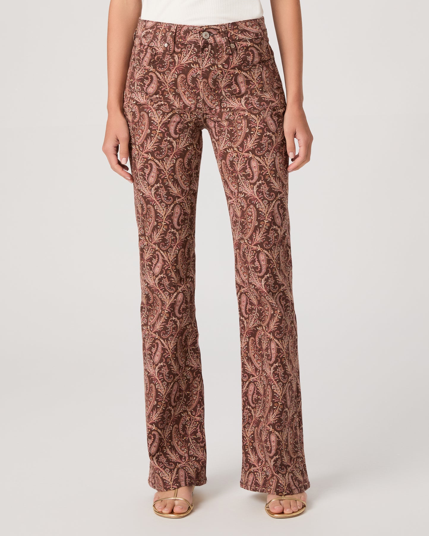 Woman wearing a white off-shoulder top and brown patterned pants on a white background