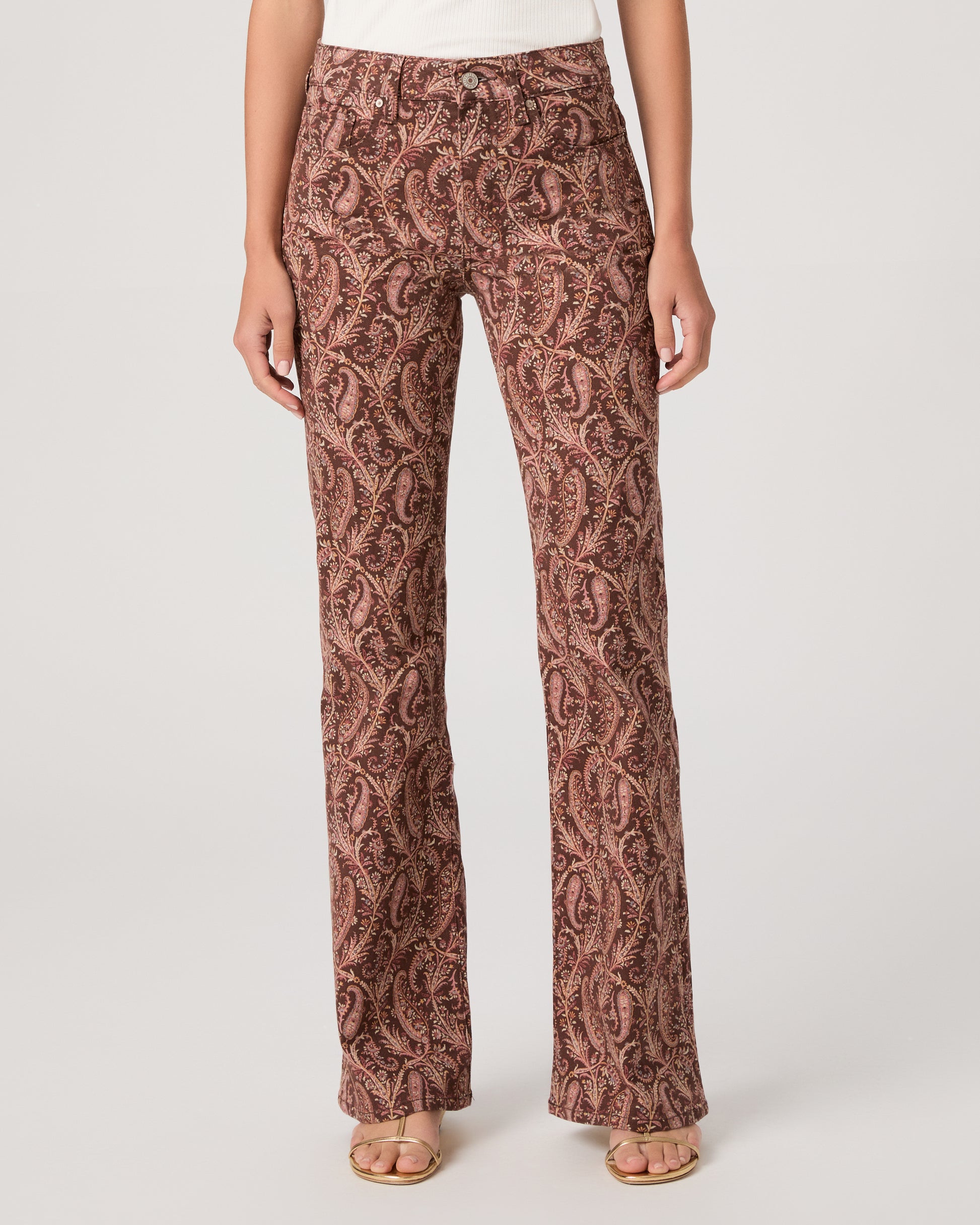 Woman wearing a white off-shoulder top and brown patterned pants on a white background