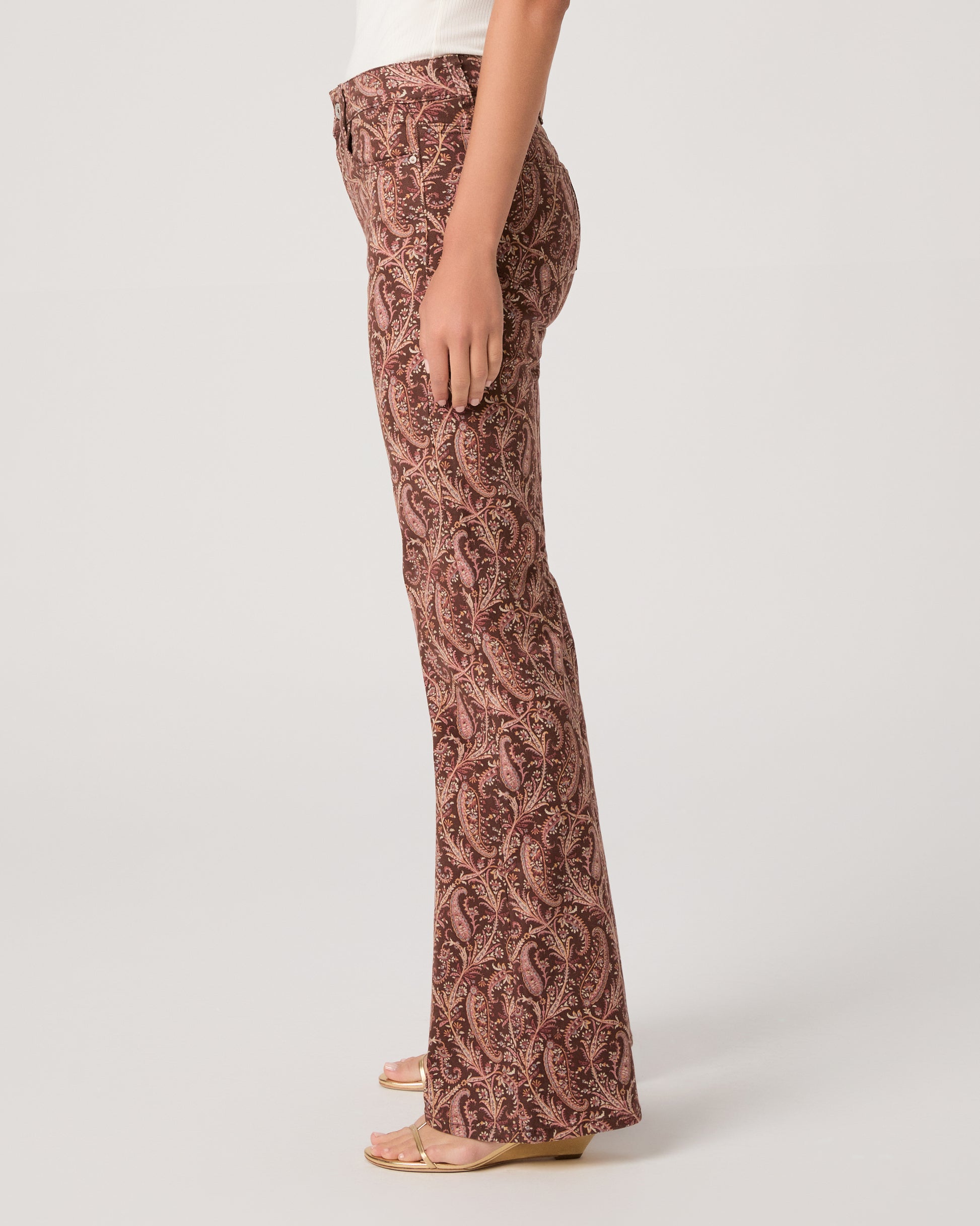 Woman wearing a white off-shoulder top and brown patterned pants on a white background