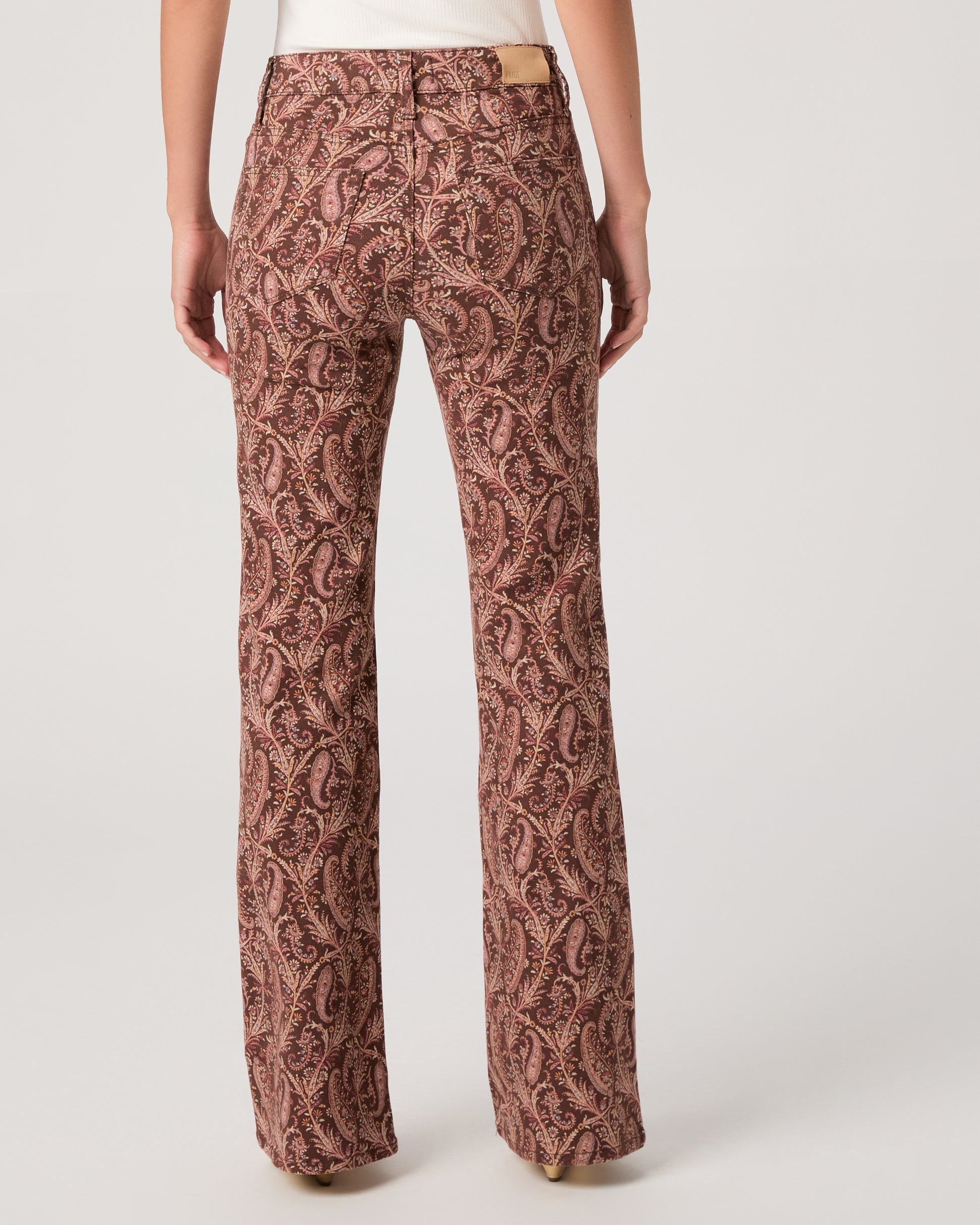 Woman wearing a white off-shoulder top and brown patterned pants on a white background