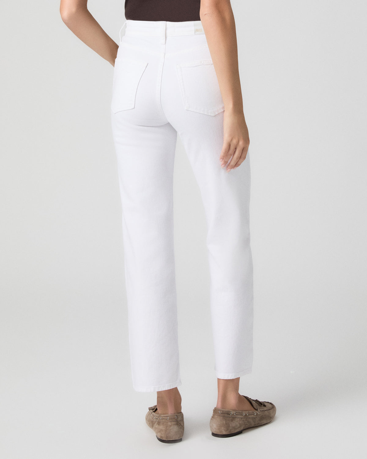 Back view from the waist down of model in a brown top, showing the back pockets and straight ankle-length leg of Stevie Jeans in Radiant White with taupe loafers