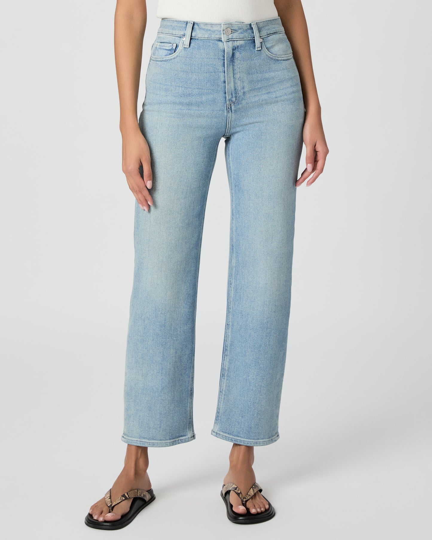 Woman wearing light blue jeans and a white top on a white background