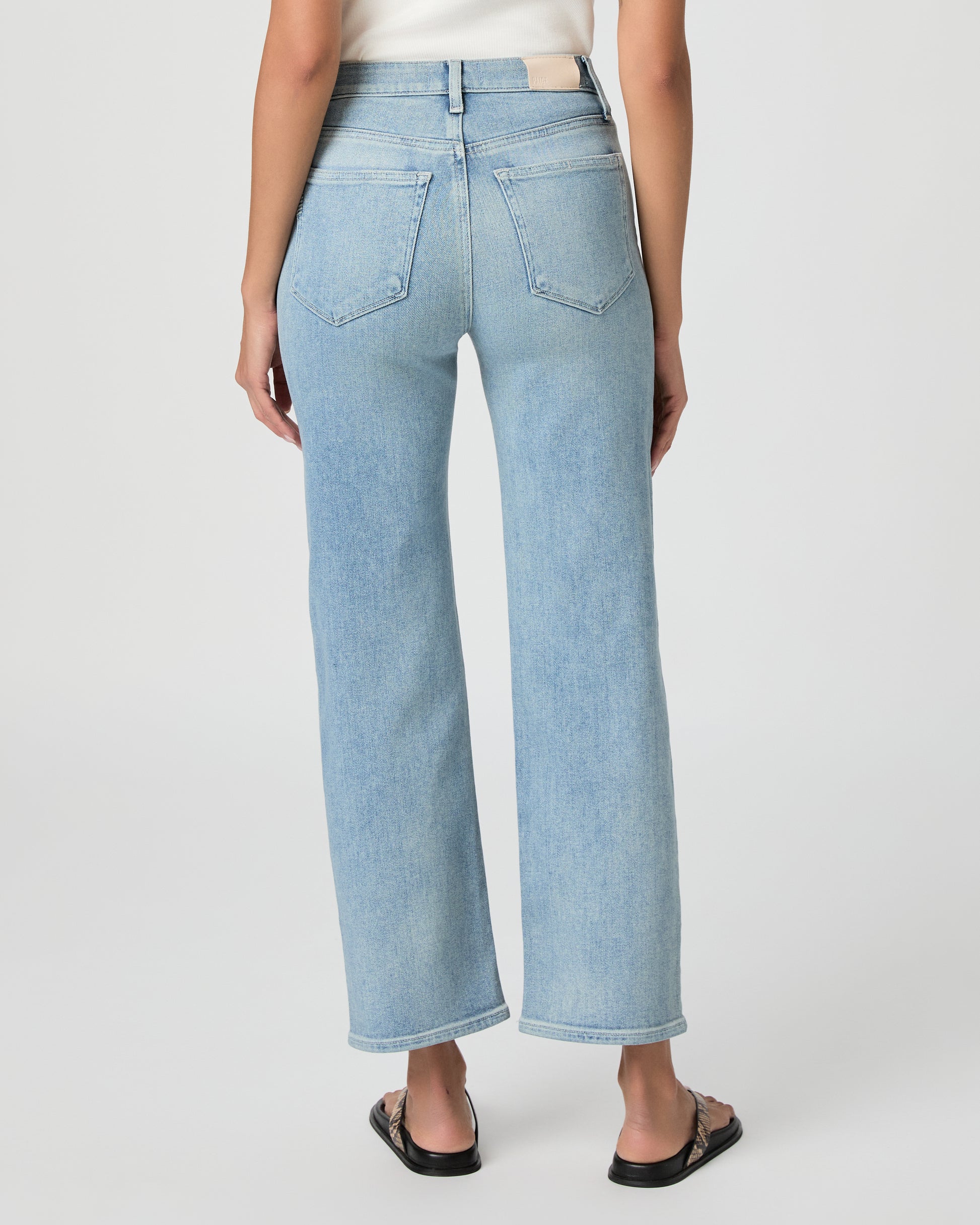 Woman wearing light blue jeans and a white top on a white background