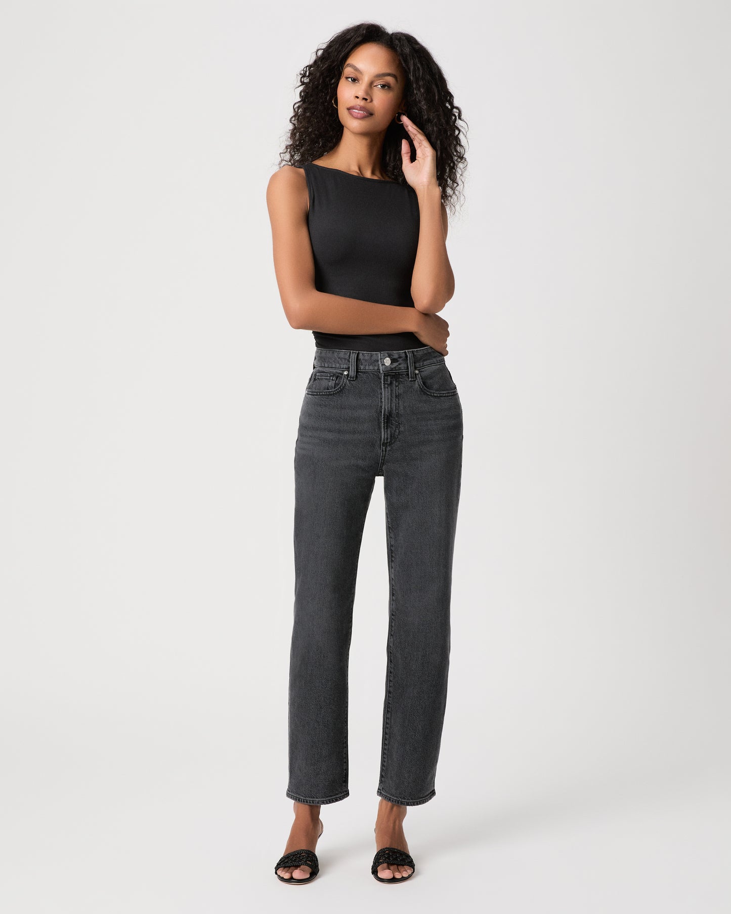 Women wearing a black top, black jeans and black heeled sandals standing against a white background 