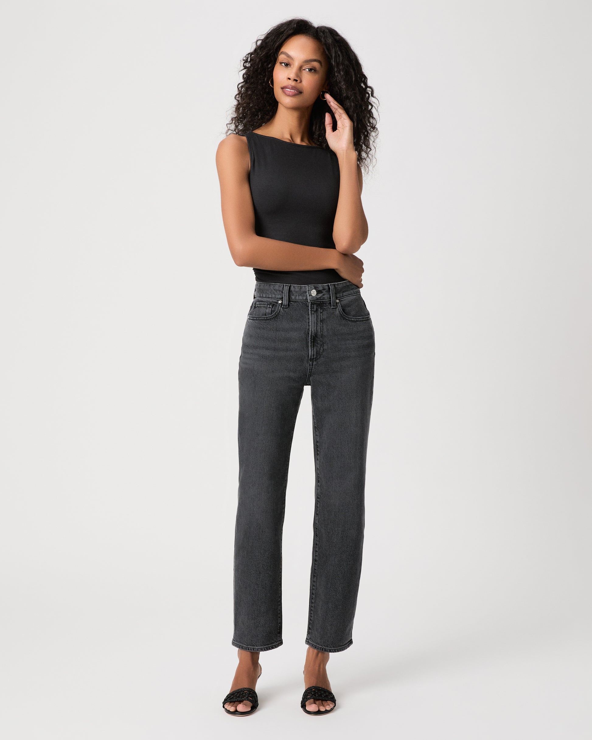 Women wearing a black top, black jeans and black heeled sandals standing against a white background 