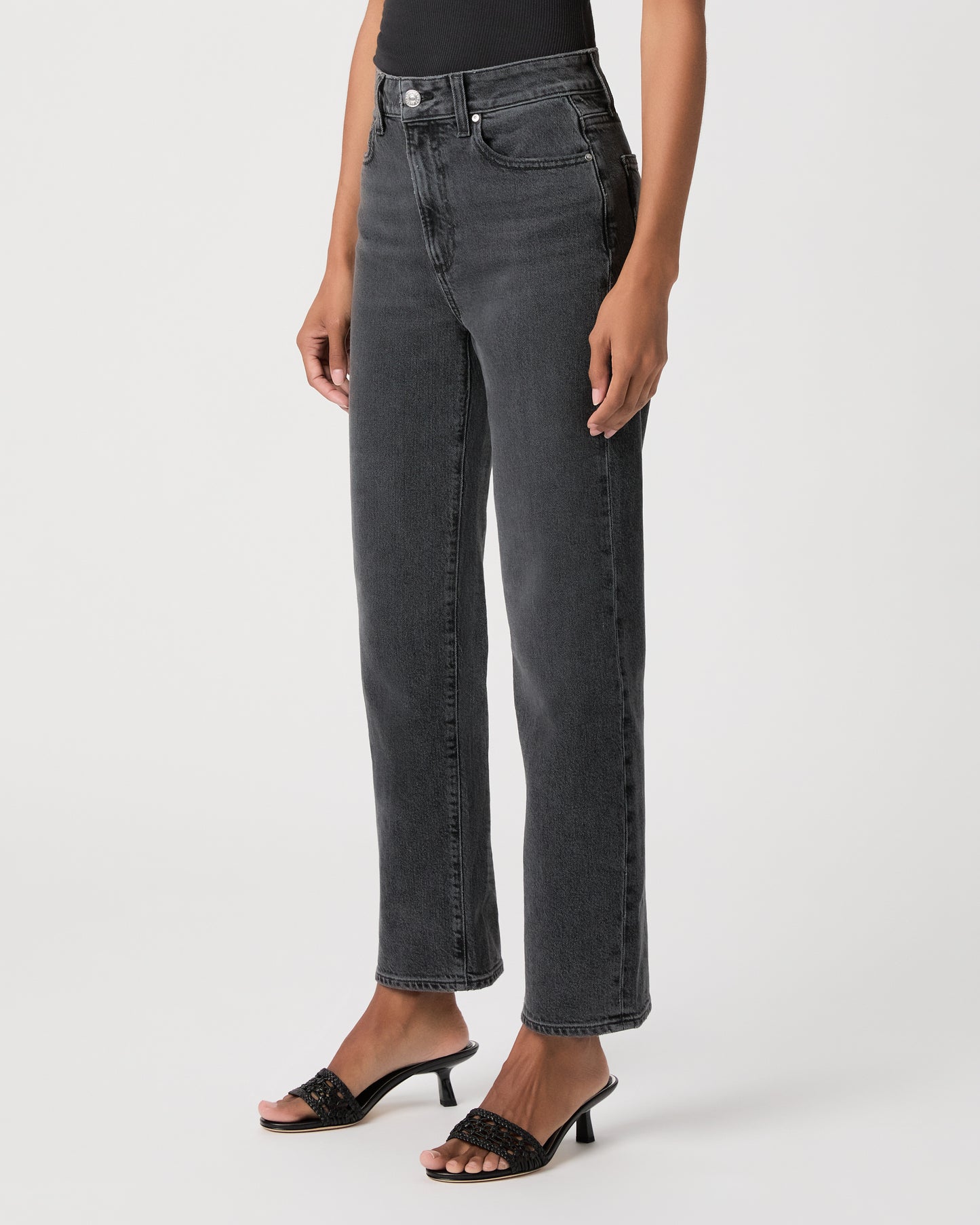 Women wearing a black top, black jeans and black heeled sandals standing against a white background 