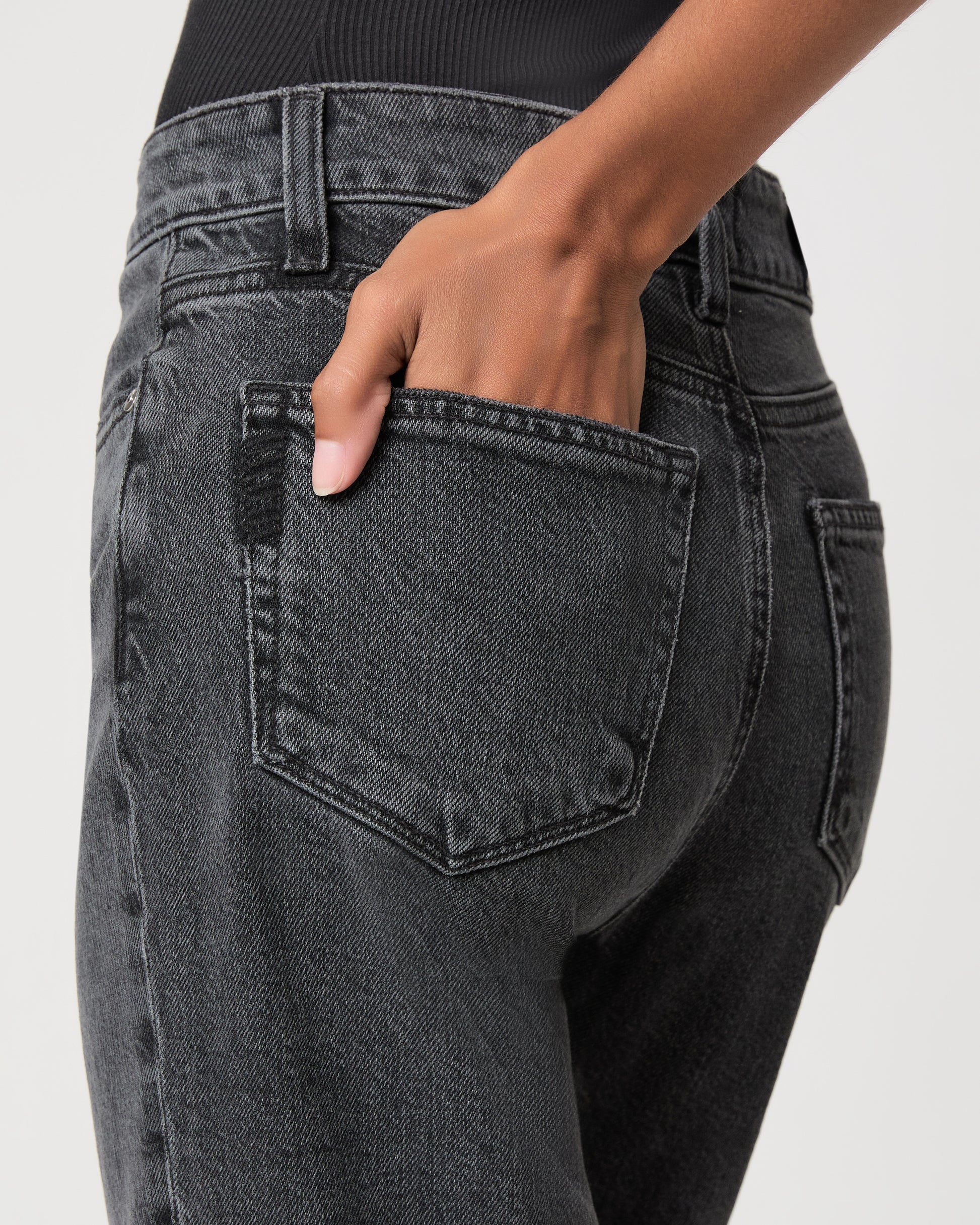 Women wearing a black top, black jeans and black heeled sandals standing against a white background 
