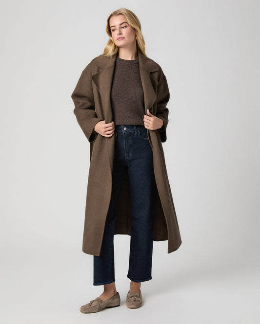 Stevie Ankle Straight Jean in Moderne dark wash; model stands facing forward holding the lapels of an open brown coat, with a brown sweater and taupe suede loafers