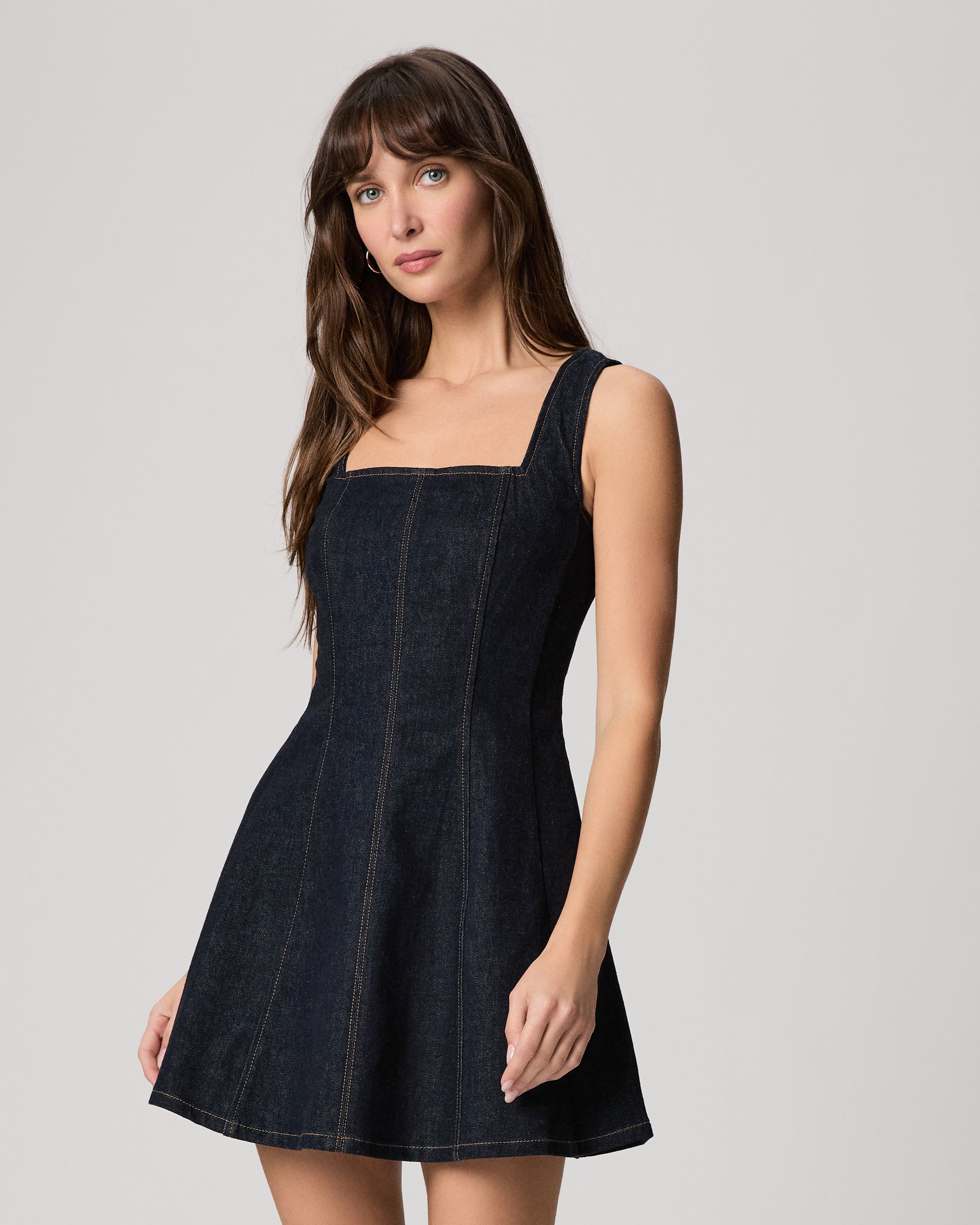 Woman wearing a dark wash denim dress on a white background