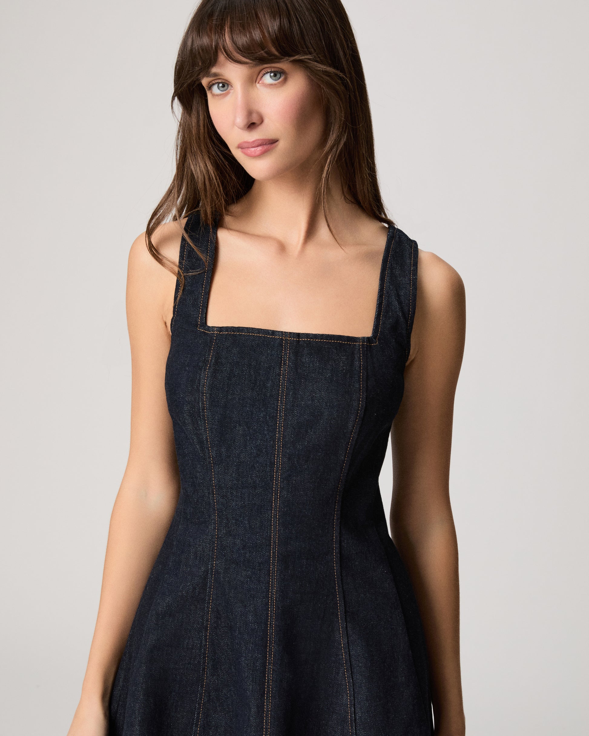 Woman wearing a dark wash denim dress on a white background