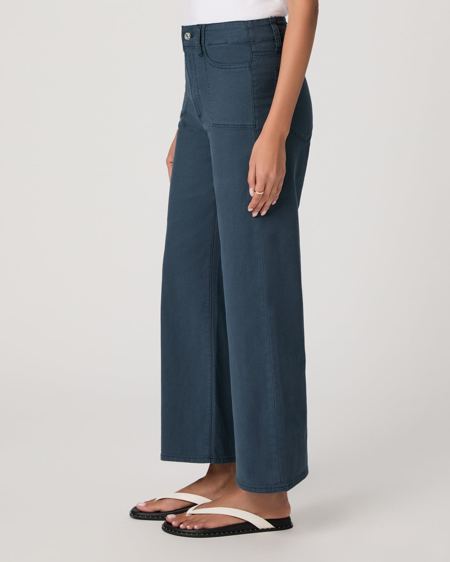 Woman wearing a white t-shirt and blue pants paired with white sandals on a plain background