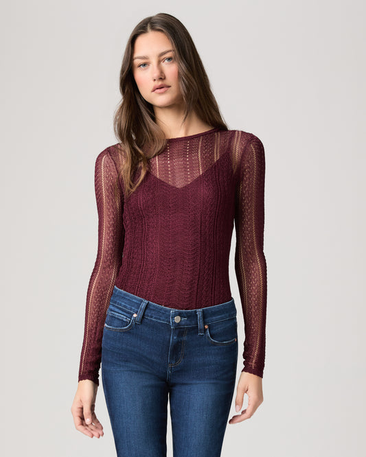 Woman wearing a burgundy long-sleeve top and blue jeans on a light gray background