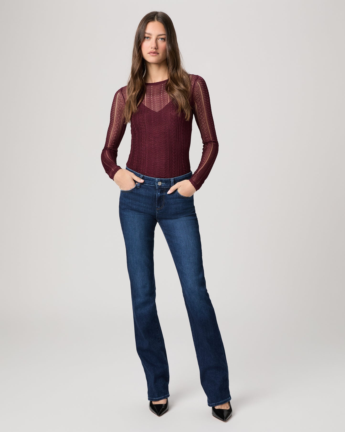 Woman wearing a burgundy long-sleeve top and blue jeans on a white background