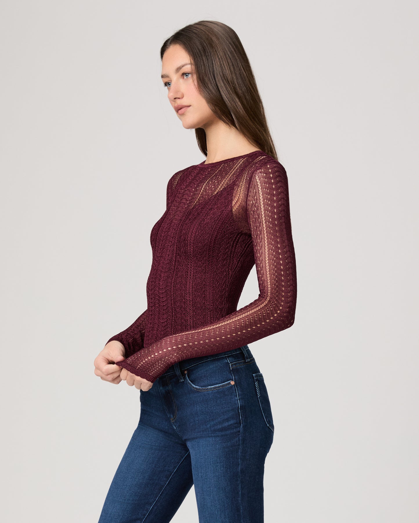 Woman wearing a burgundy sweater with sheer sleeves against a light gray background