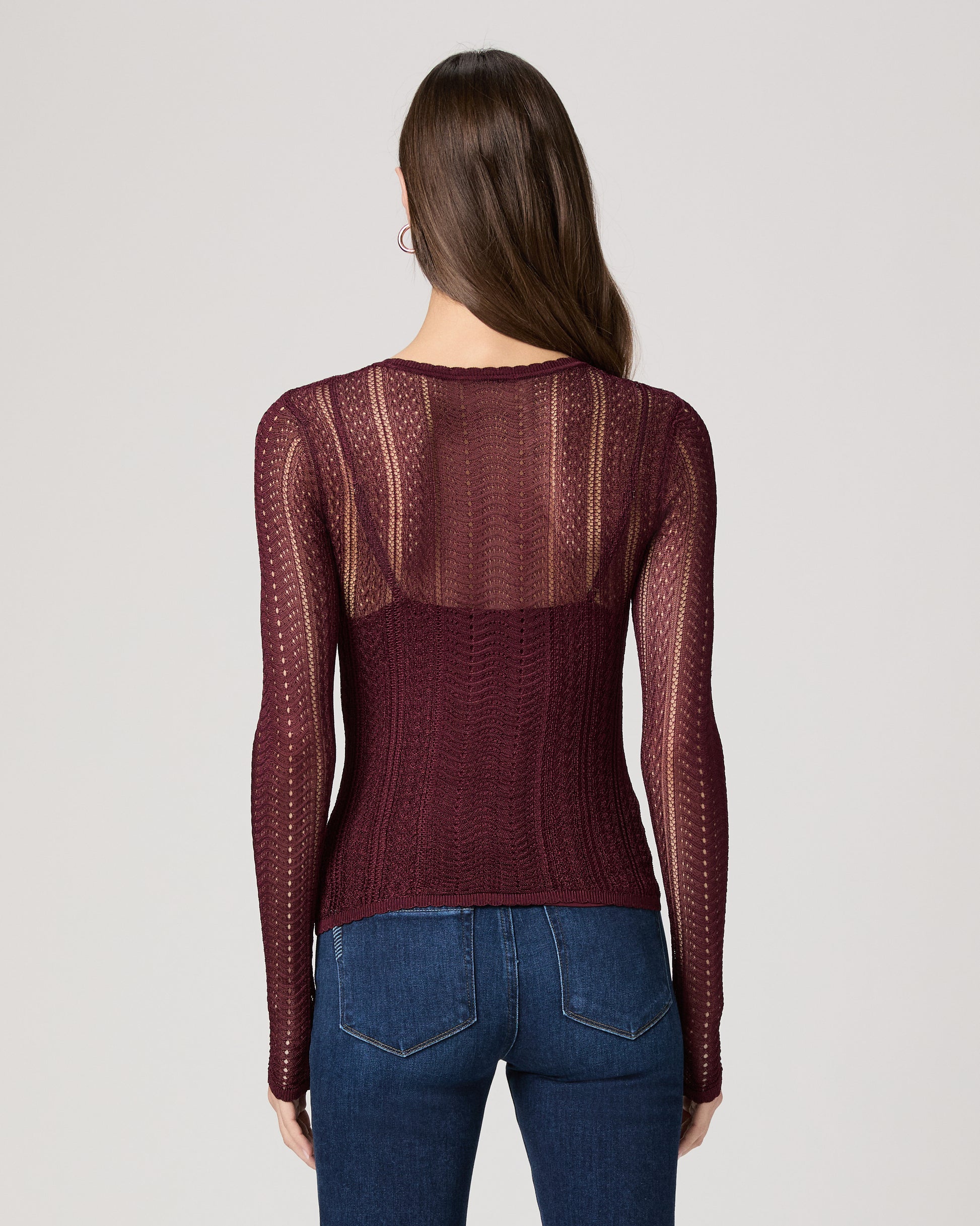 Woman wearing a burgundy sweater with sheer sleeves on a light gray background