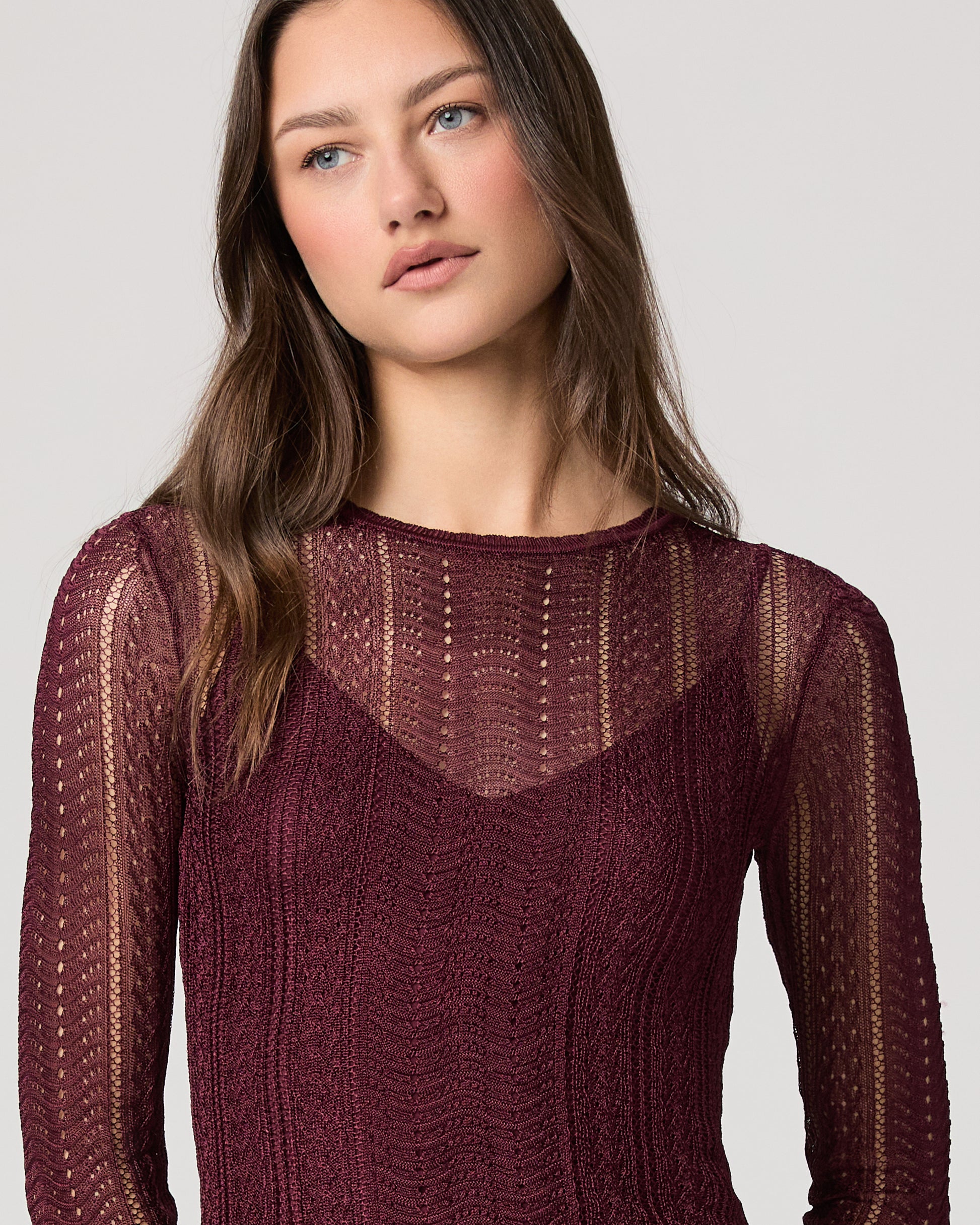 Woman wearing a maroon sweater with intricate patterns on a plain background