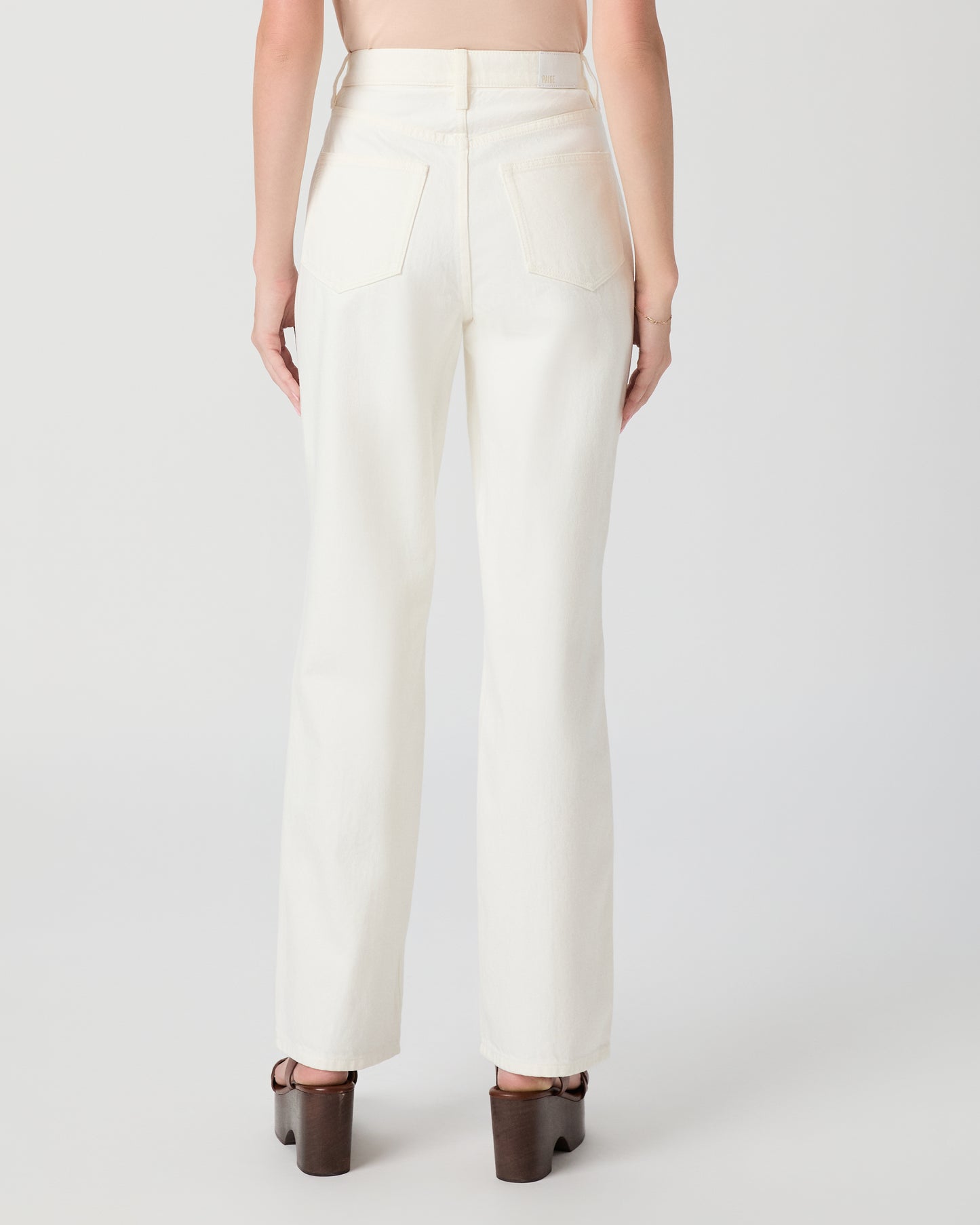 Woman wearing a pink top and white pants paired with brown heels on a plain background