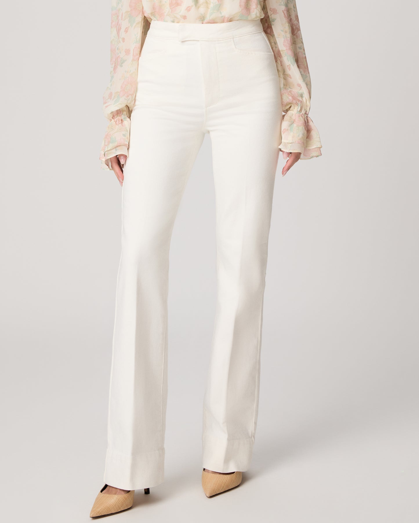 Woman wearing a floral blouse and white pants on a plain background