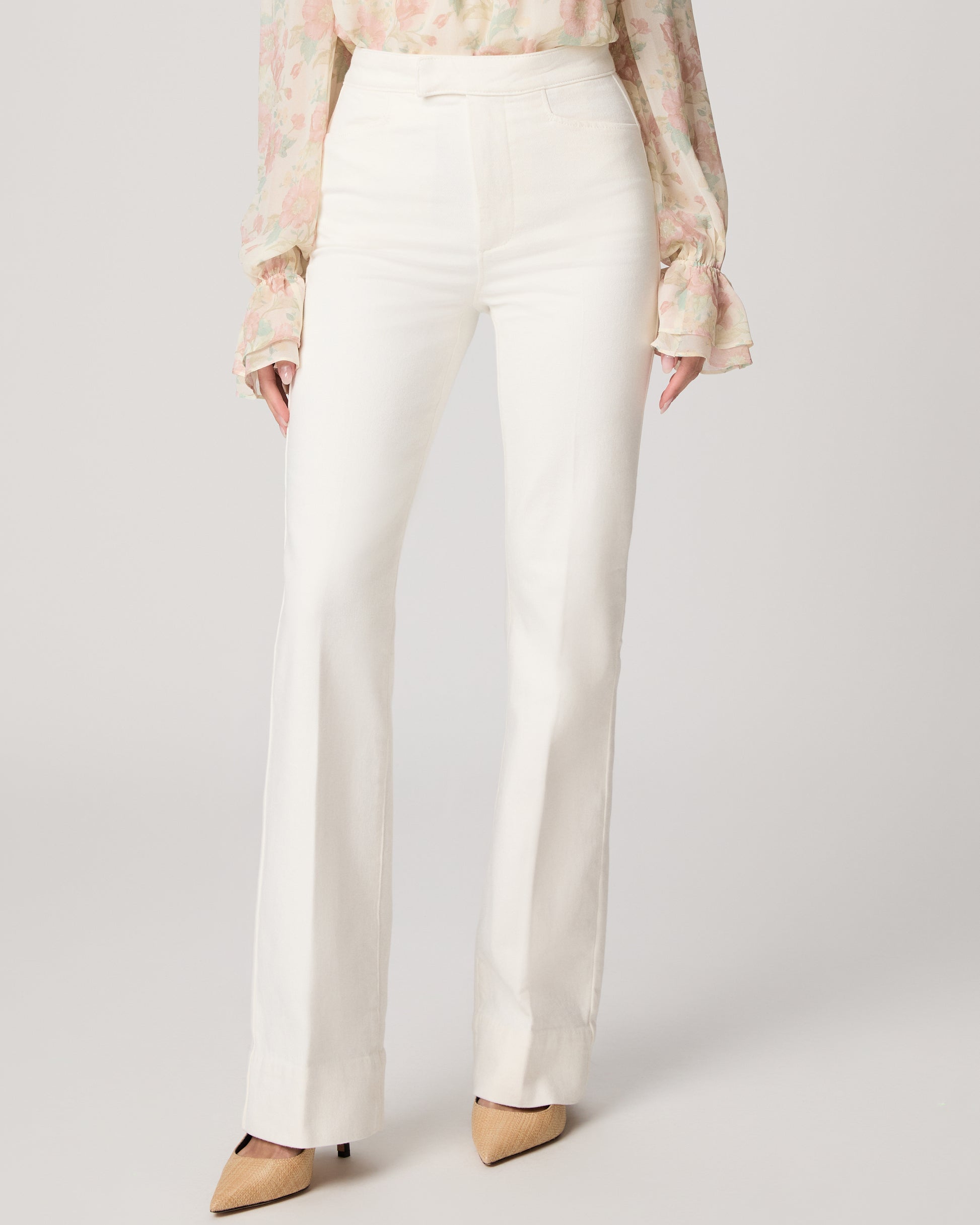 Woman wearing a floral blouse and white pants on a plain background