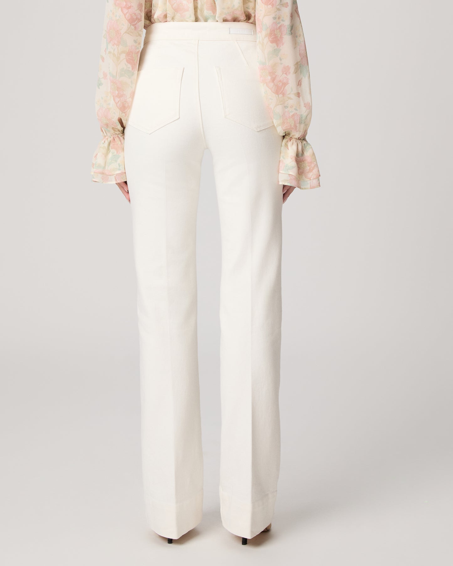 Woman wearing a floral blouse and white pants on a plain background