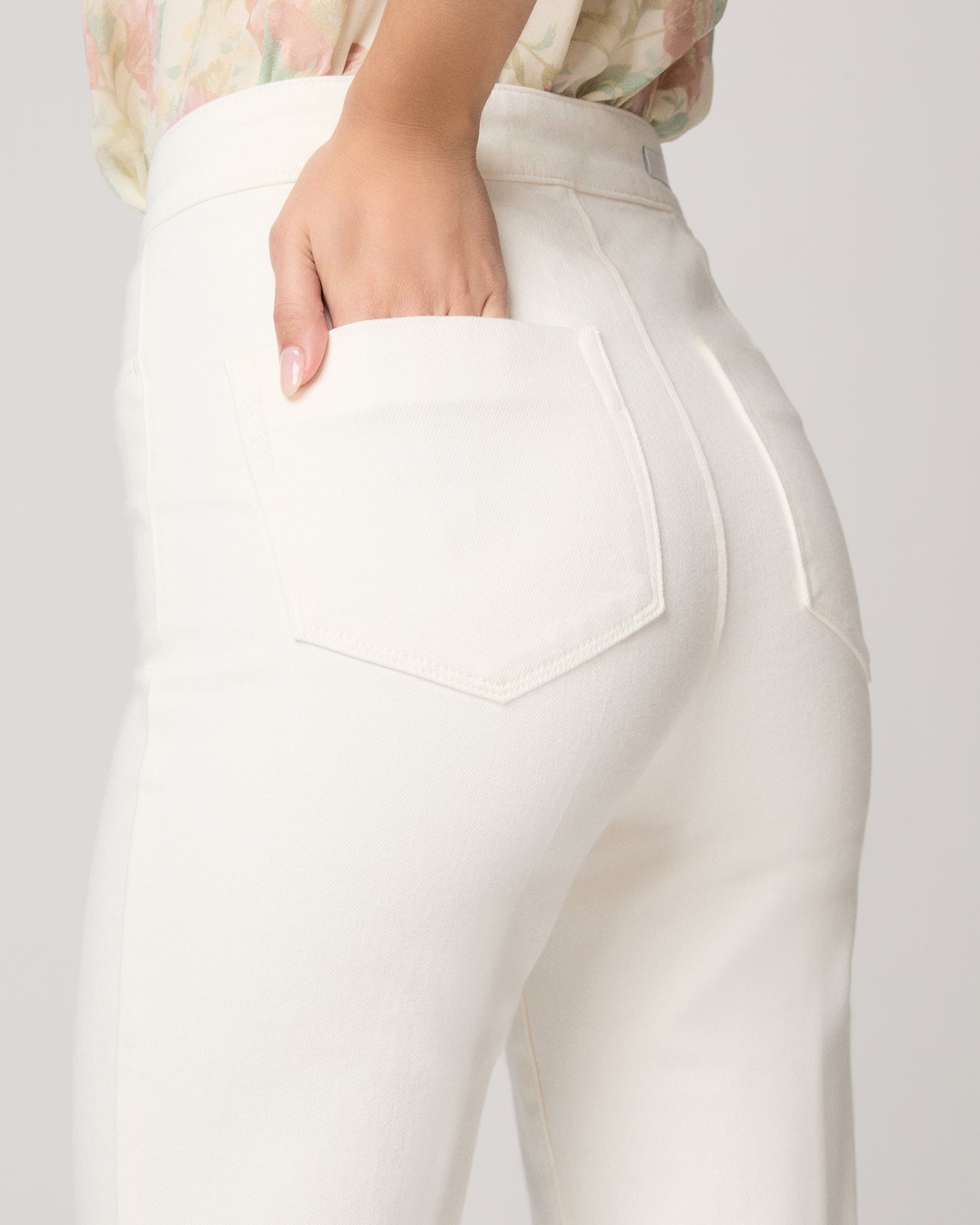 Woman wearing a floral blouse and white pants on a plain background