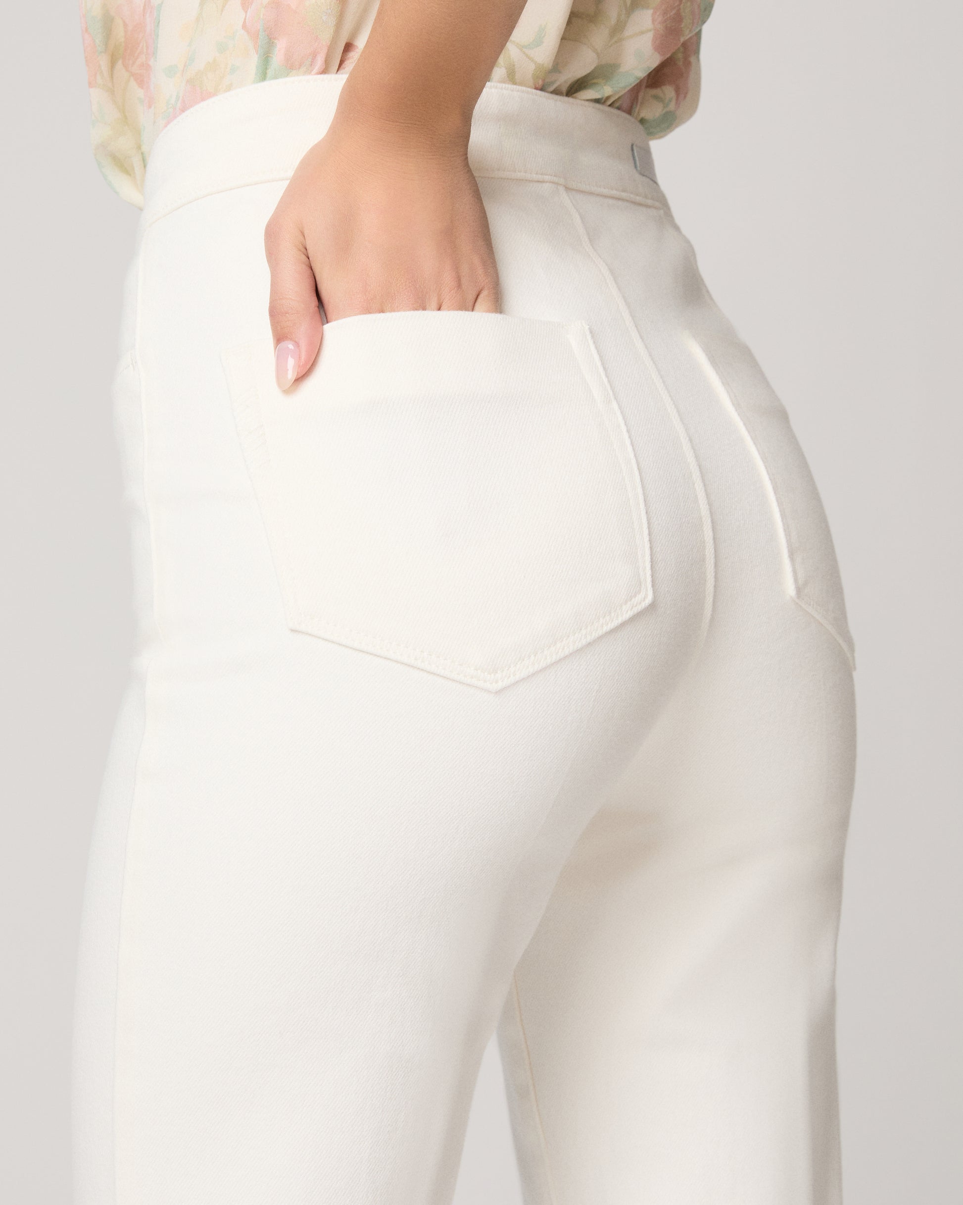 Woman wearing a floral blouse and white pants on a plain background