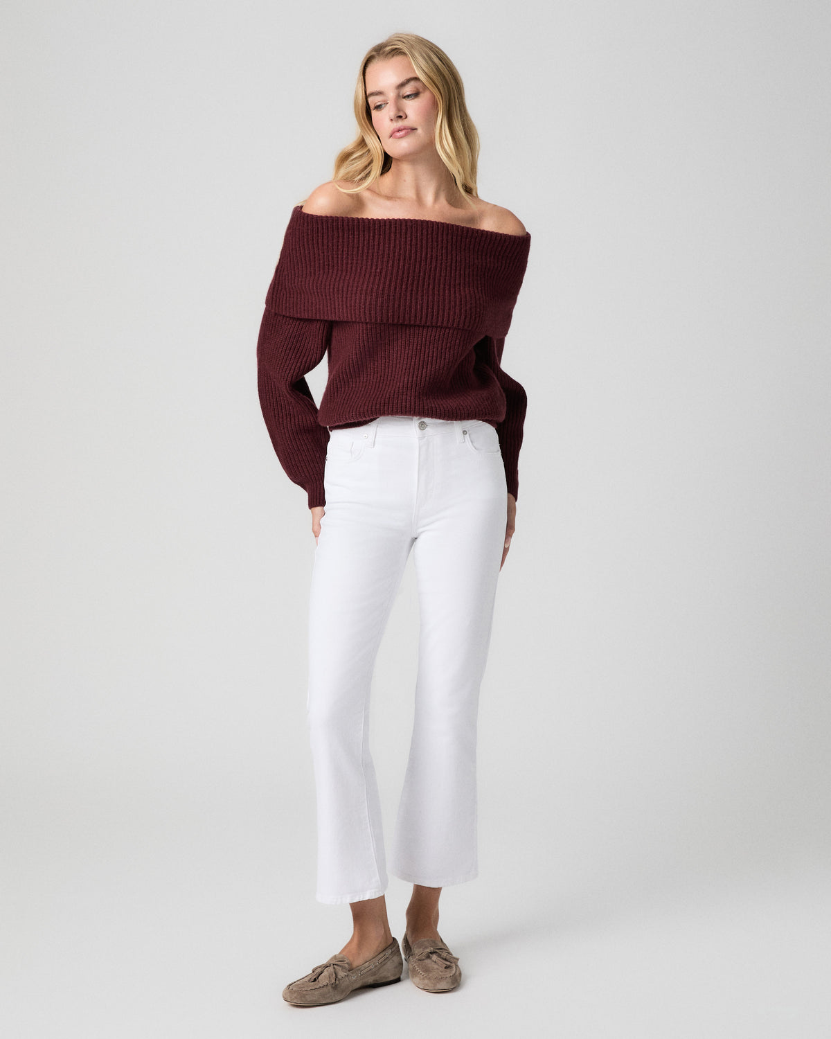 Model standing facing forward, arms at her sides, wearing a burgundy off-the-shoulder knit sweater, Mason Crop Bootcut Jeans in Radiant White, and taupe suede loafers
