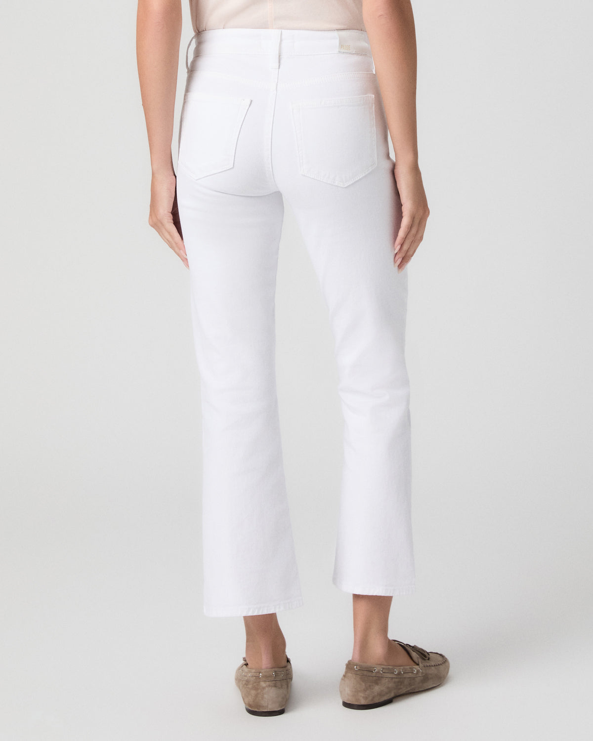 Back view from the waist down of model in a blush top, showing the back pockets and cropped bootcut leg of Mason Jeans in Radiant White with taupe loafers