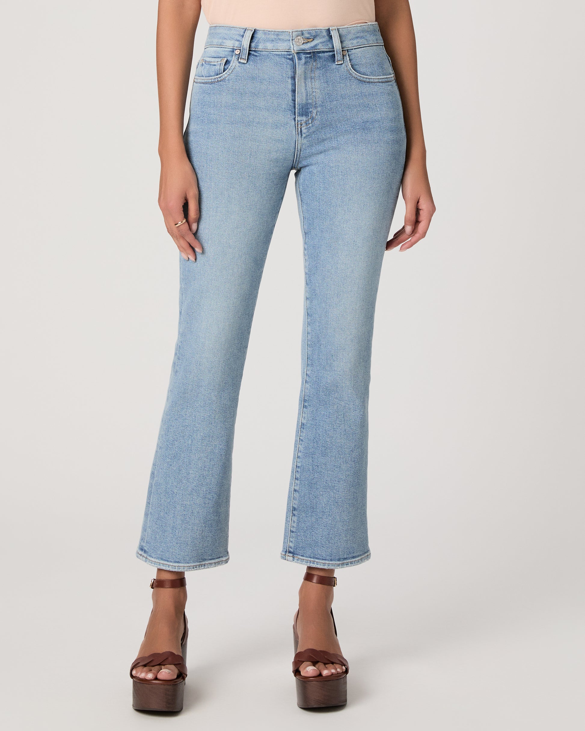 Woman wearing a beige top and blue jeans on a white background