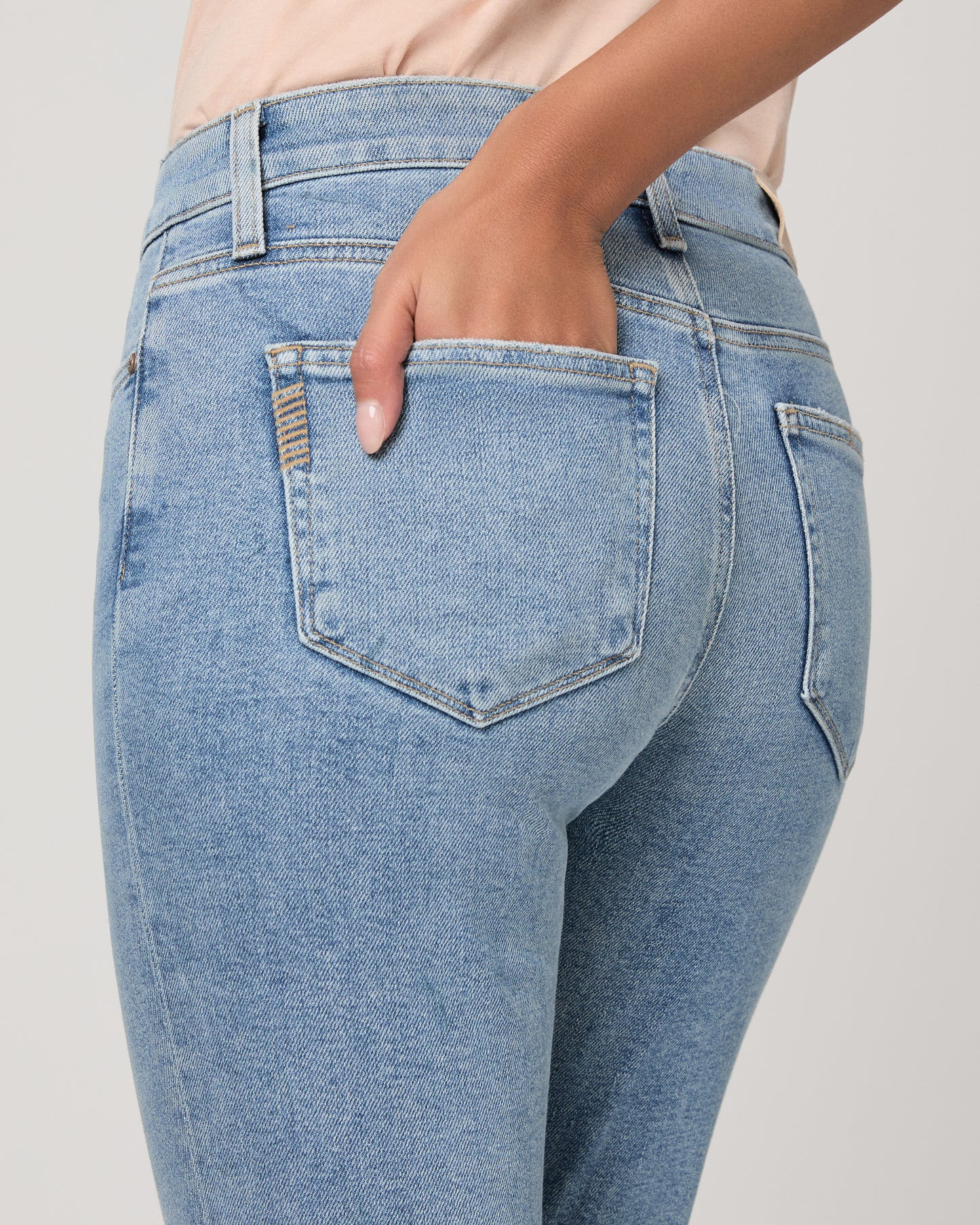 Woman wearing a beige top and blue jeans on a white background