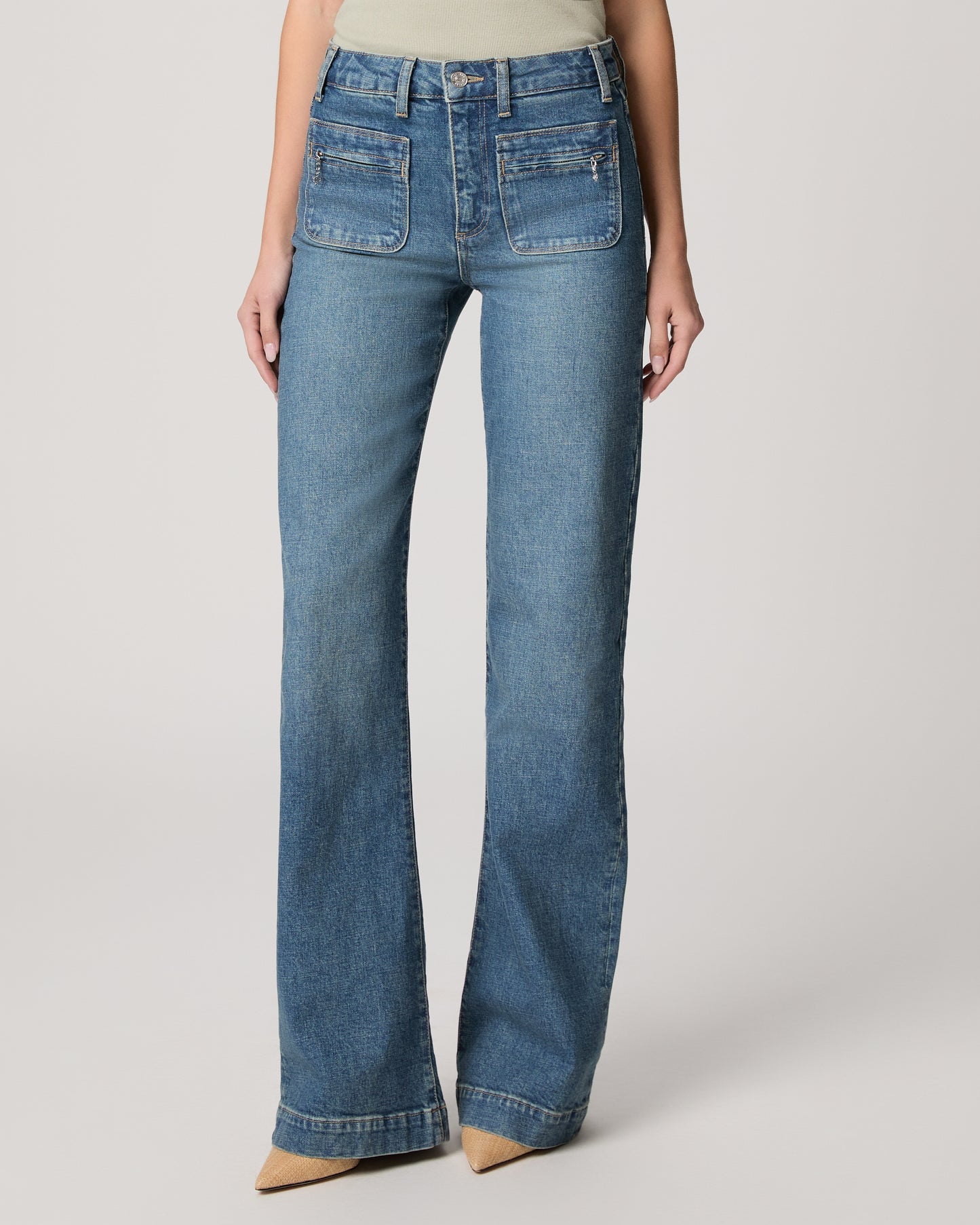 Woman wearing a light green blouse and blue jeans on a plain background