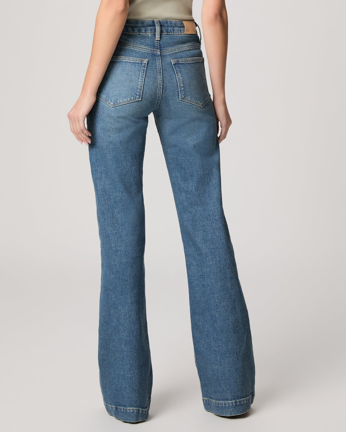 Woman wearing a light green blouse and blue jeans on a plain background