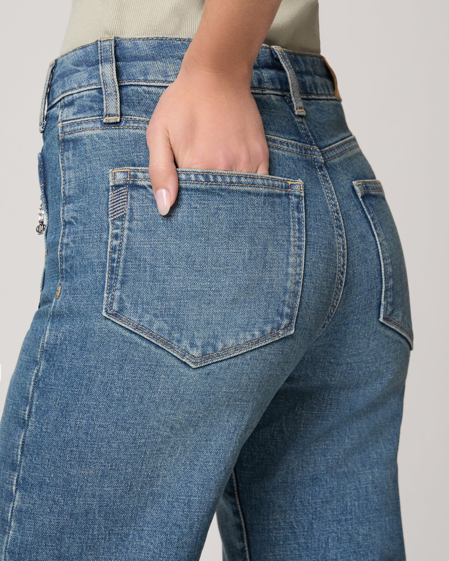 Woman wearing a light green blouse and blue jeans on a plain background