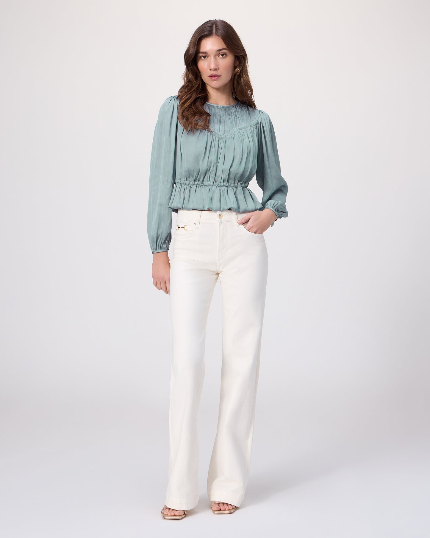 Woman wearing a teal blouse and white pants on a white background